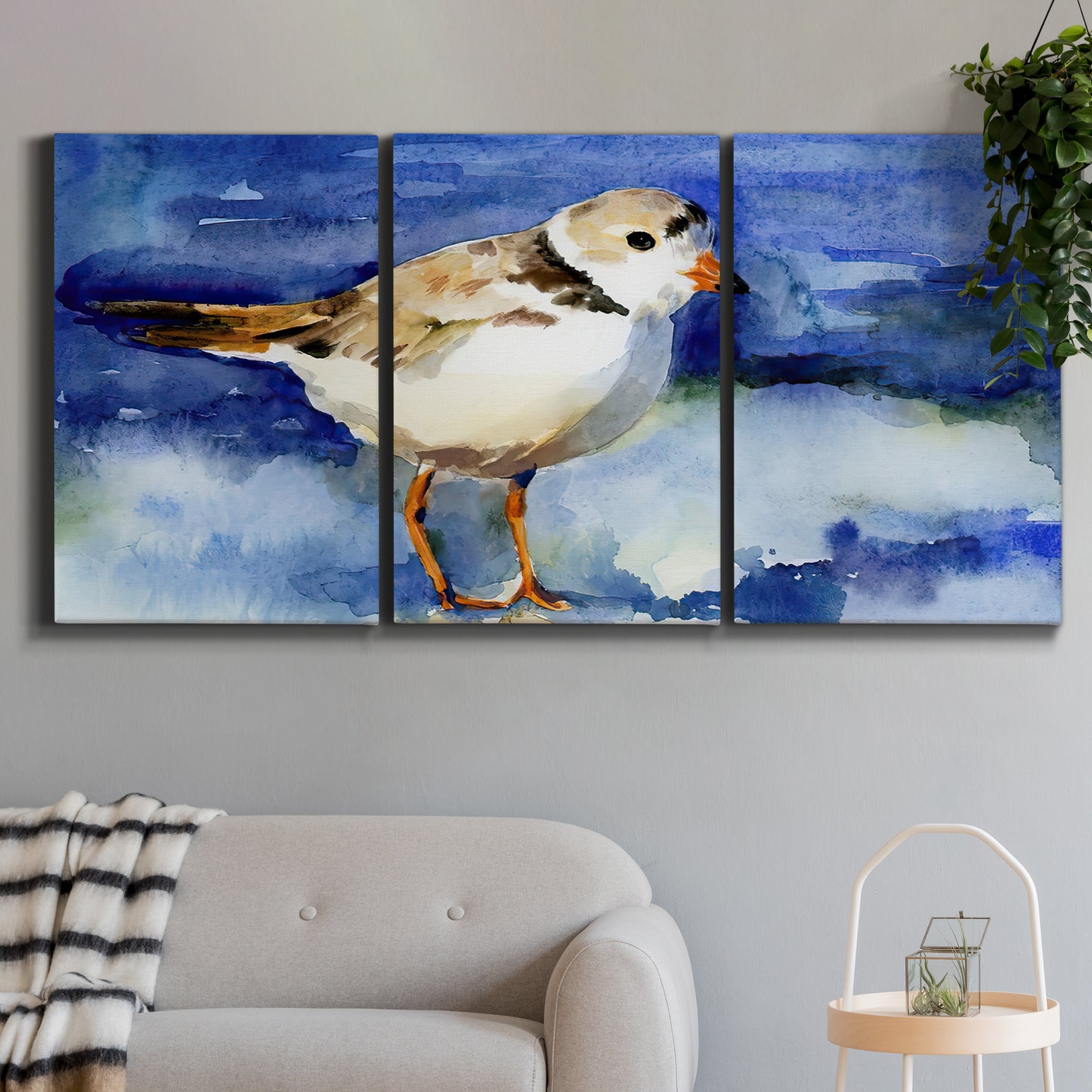 Three-panel canvas wall art featuring shorebirds standing in shallow water, displayed in a modern living room above a sofa.
