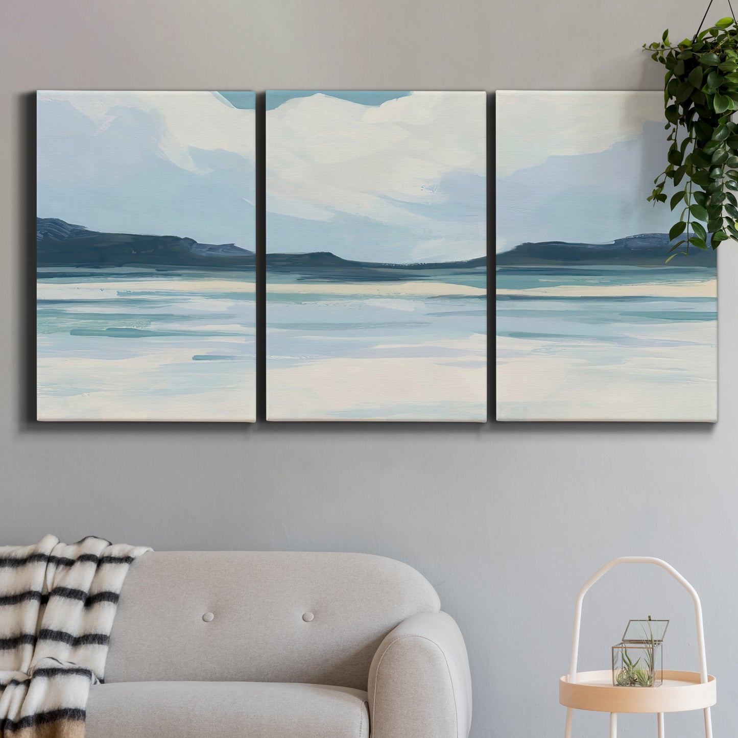Three-panel canvas wall art featuring soft coastal shoreline landscape, displayed in a modern living room above a sofa.