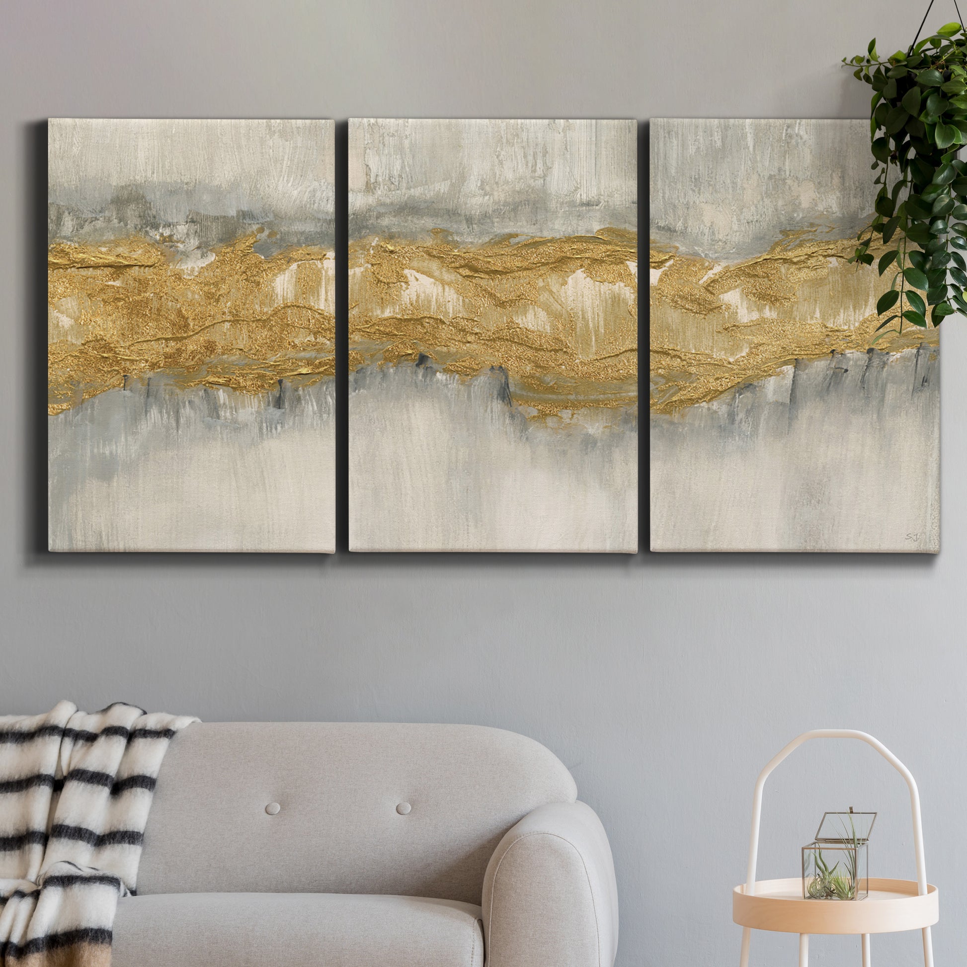 Three-panel canvas wall art featuring flowing abstract golden tones, displayed in a modern living room above a sofa.
