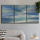 Three-panel canvas wall art featuring sunbeams breaking through coastal clouds, displayed in a modern living room above a sofa.