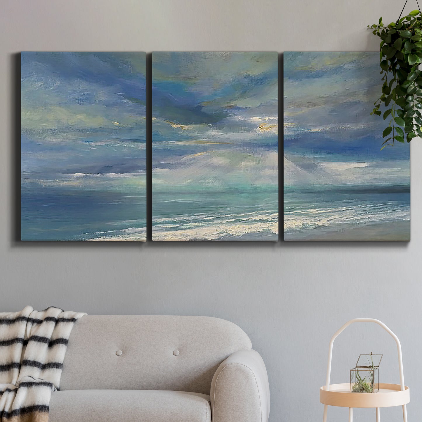 Three-panel canvas wall art featuring sunbeams breaking through coastal clouds, displayed in a modern living room above a sofa.
