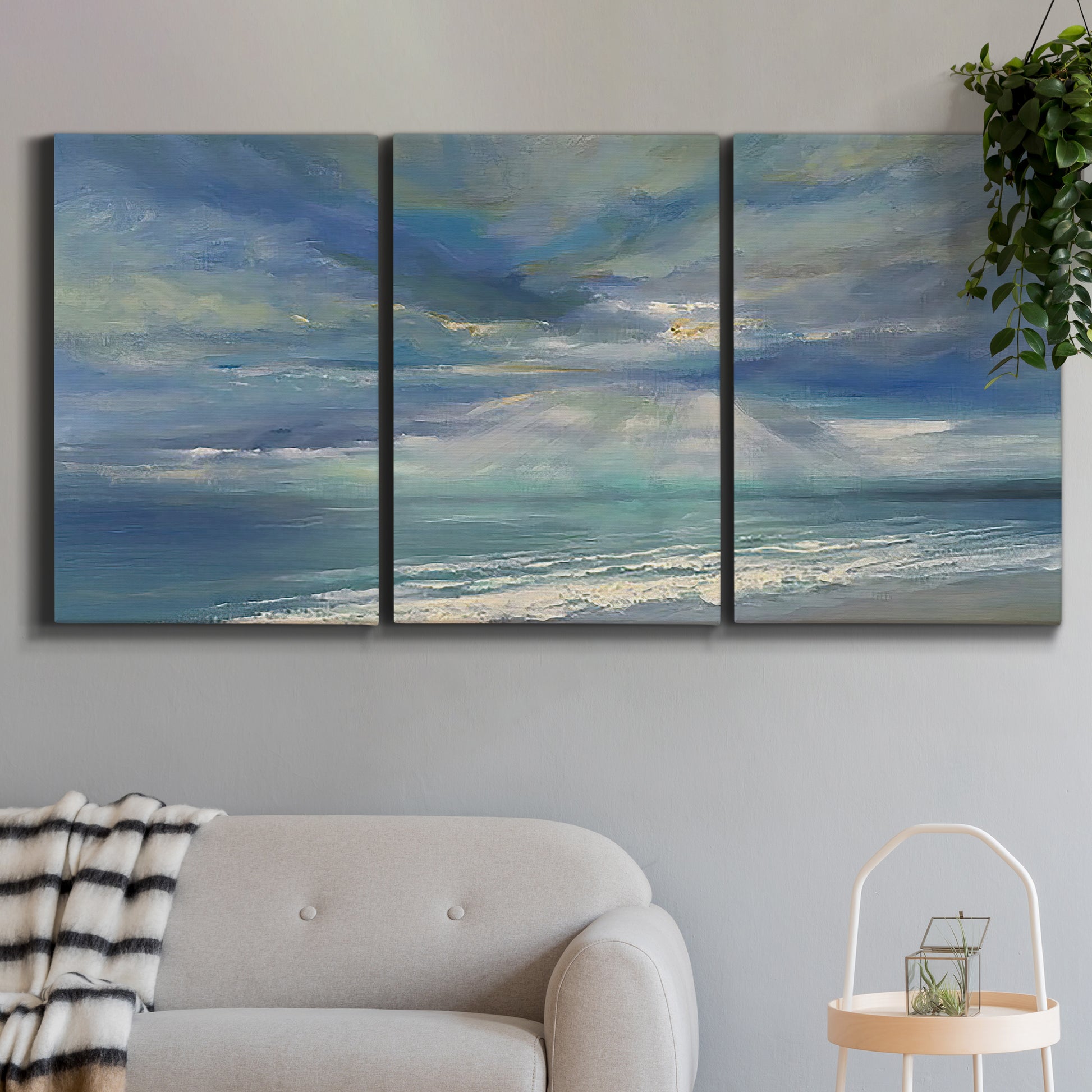 Three-panel canvas wall art featuring sunbeams breaking through coastal clouds, displayed in a modern living room above a sofa.