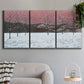Three-panel canvas wall art featuring winter sunset snowfall landscape, displayed in a modern living room above a sofa.