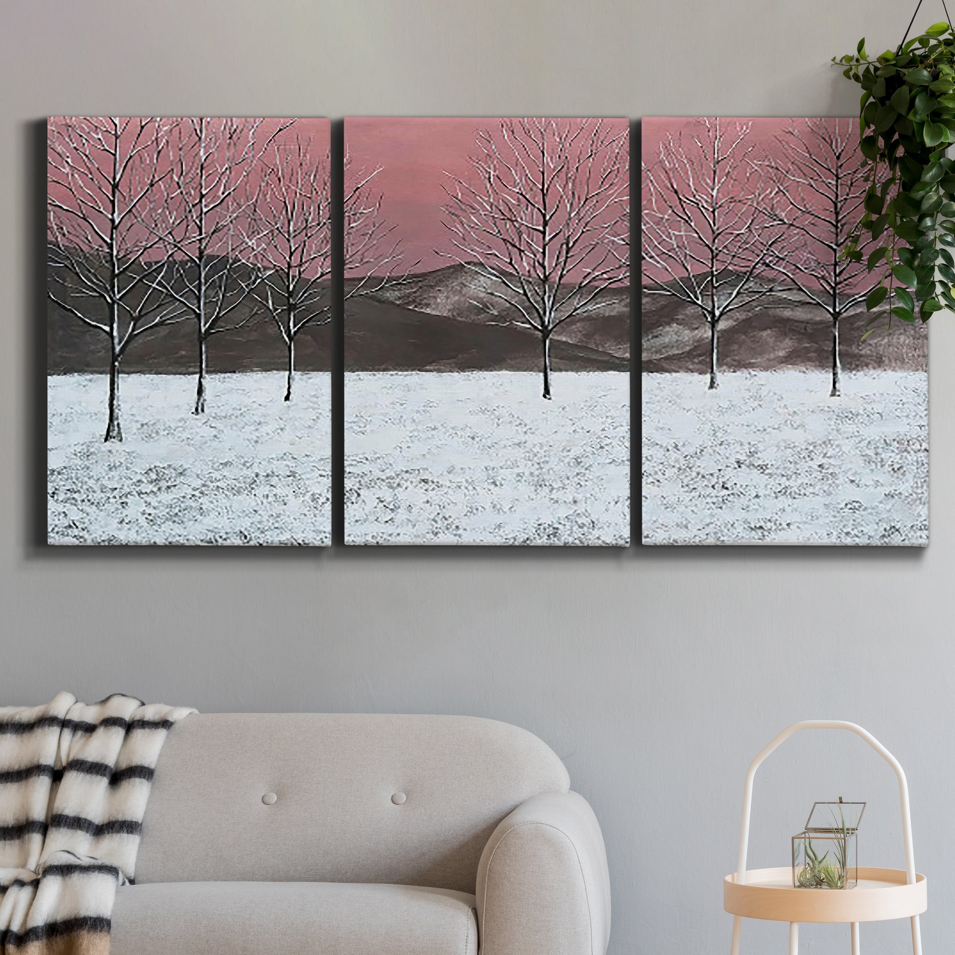 Three-panel canvas wall art featuring winter sunset snowfall landscape, displayed in a modern living room above a sofa.