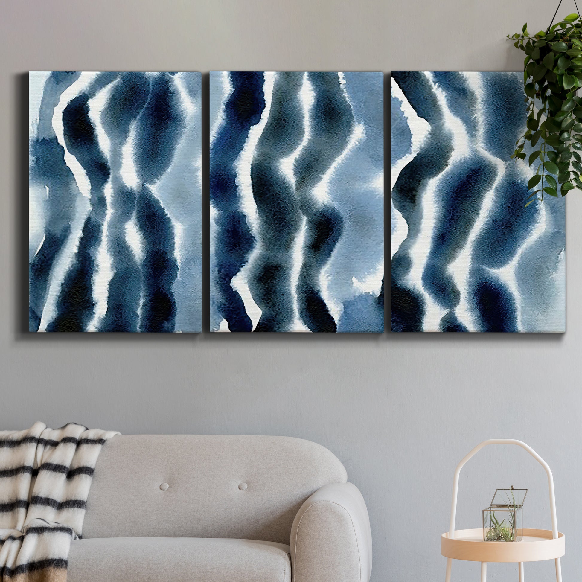 Three-panel canvas wall art featuring flowing blue watercolor wave forms, displayed in a modern living room above a sofa.