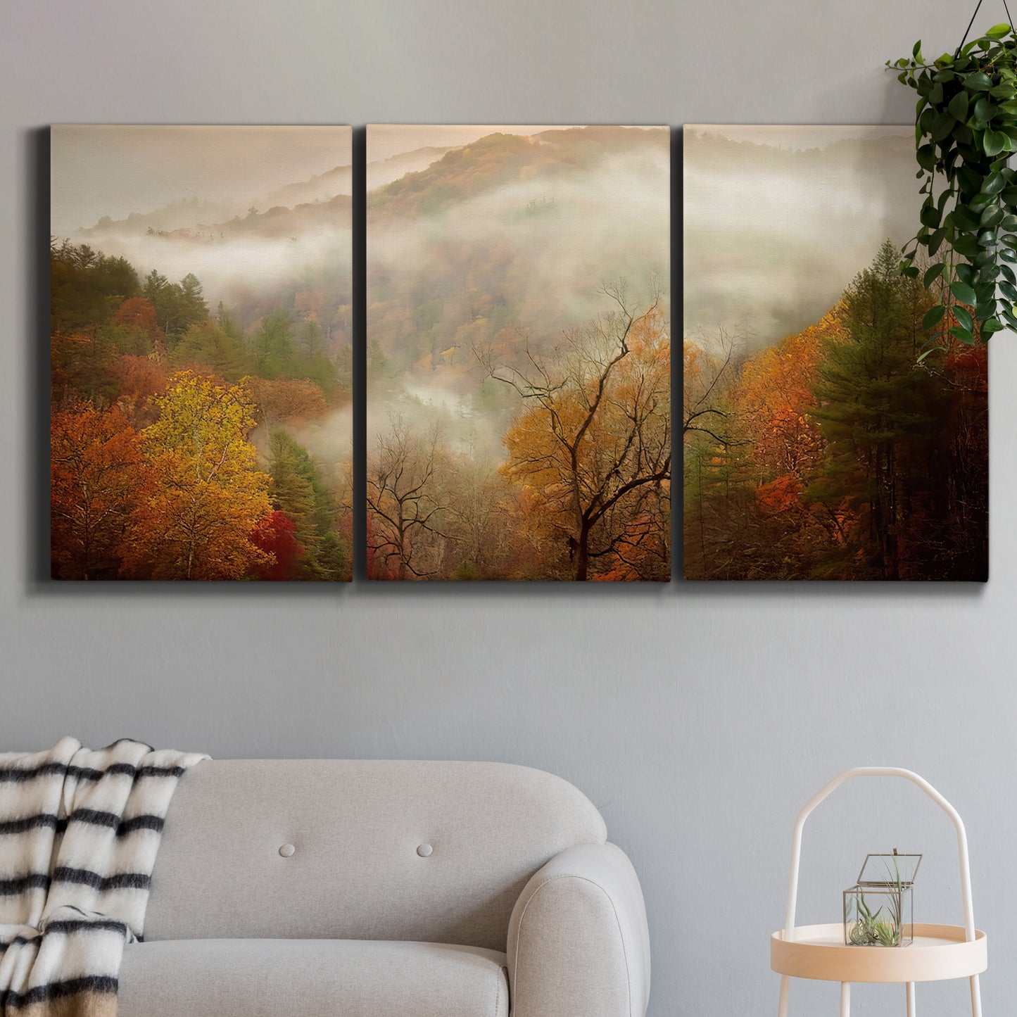 Three-panel canvas wall art featuring misty autumn landscape photograph, displayed in a modern living room above a sofa.