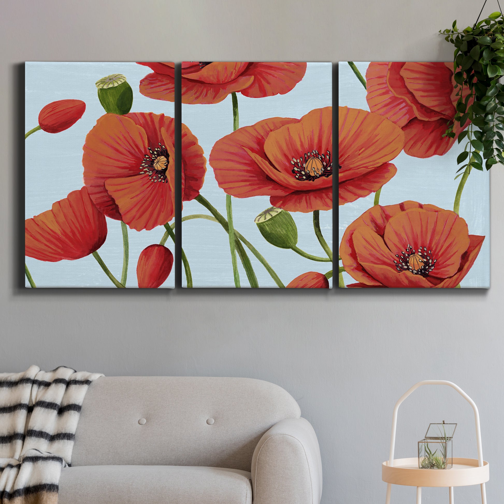 Three-panel canvas wall art featuring red poppies in motion, displayed in a modern living room above a sofa.