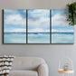 Three-panel canvas wall art featuring tropical clouds over ocean horizon, displayed in a modern living room above a sofa.