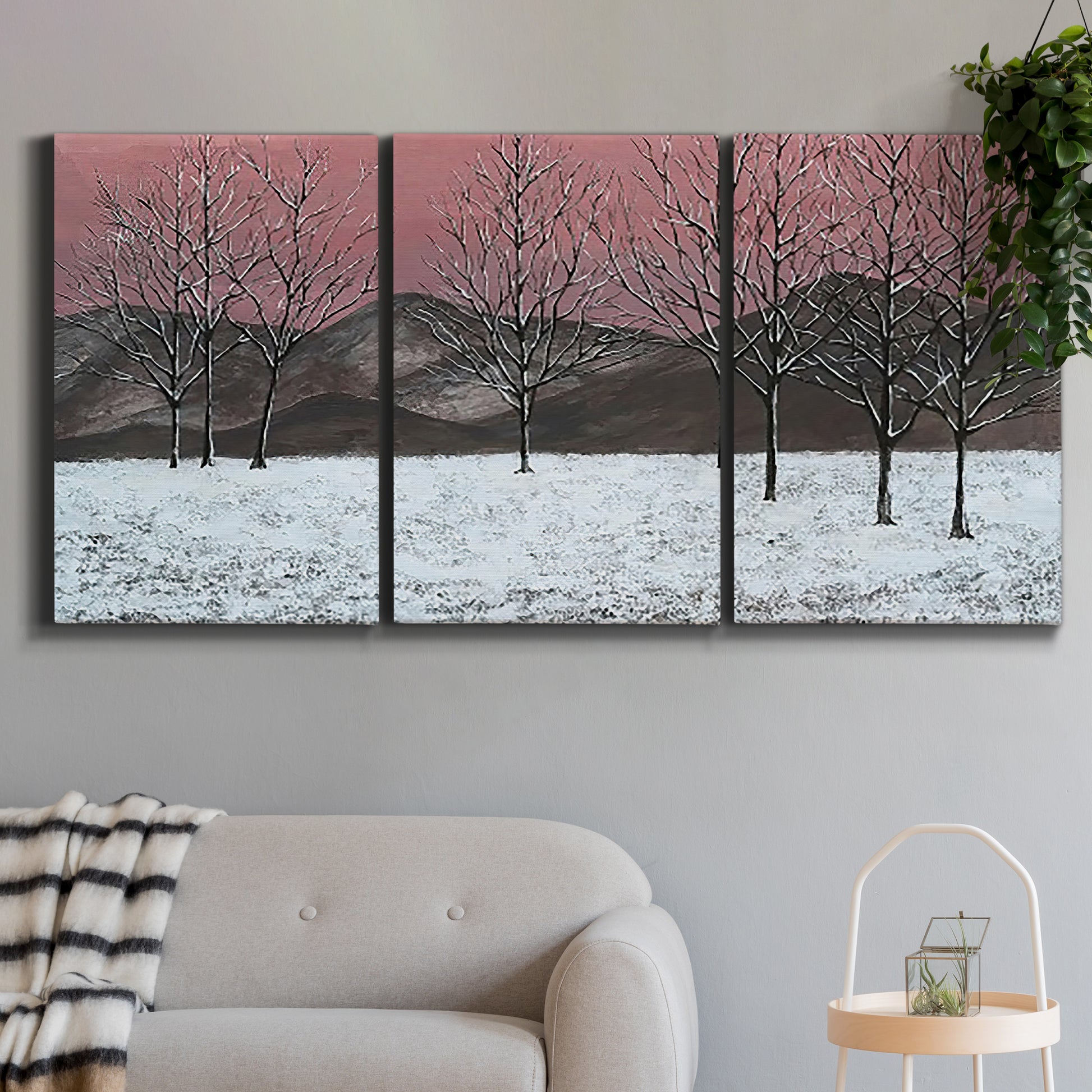 Three-panel canvas wall art featuring winter sunset snowfall landscape, displayed in a modern living room above a sofa.