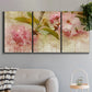 Three-panel canvas wall art featuring soft floral blossom composition, displayed in a modern living room above a sofa.