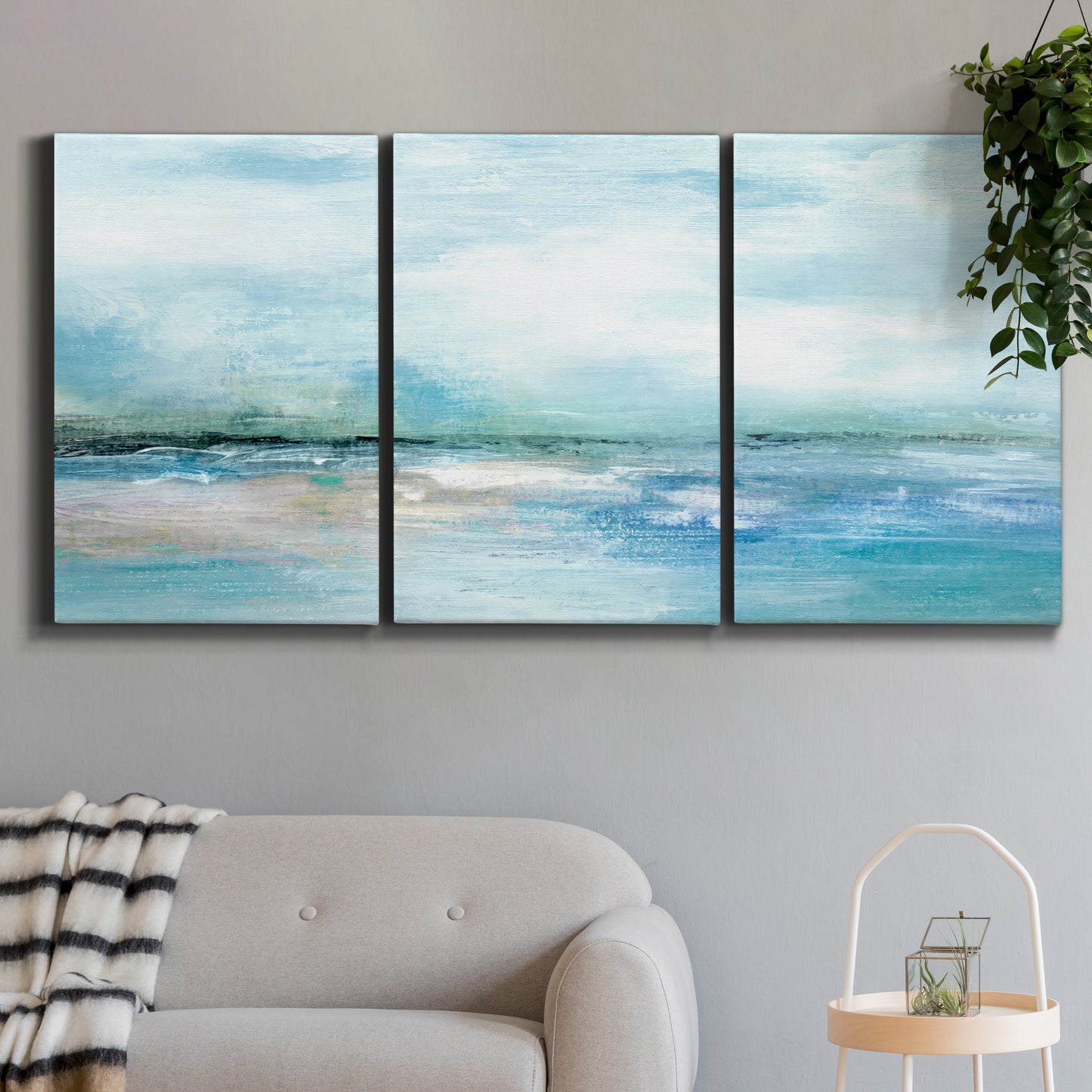 Three-panel canvas wall art featuring sunset silhouette over coastal water, displayed in a modern living room above a sofa.