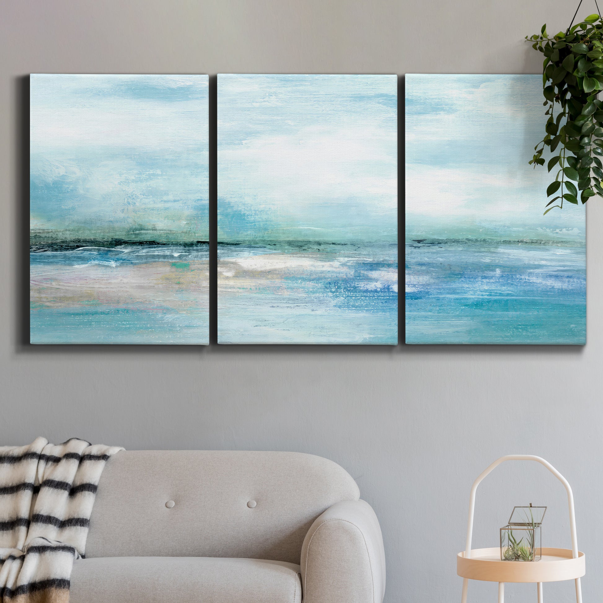 Three-panel canvas wall art featuring sunset silhouette over coastal water, displayed in a modern living room above a sofa.