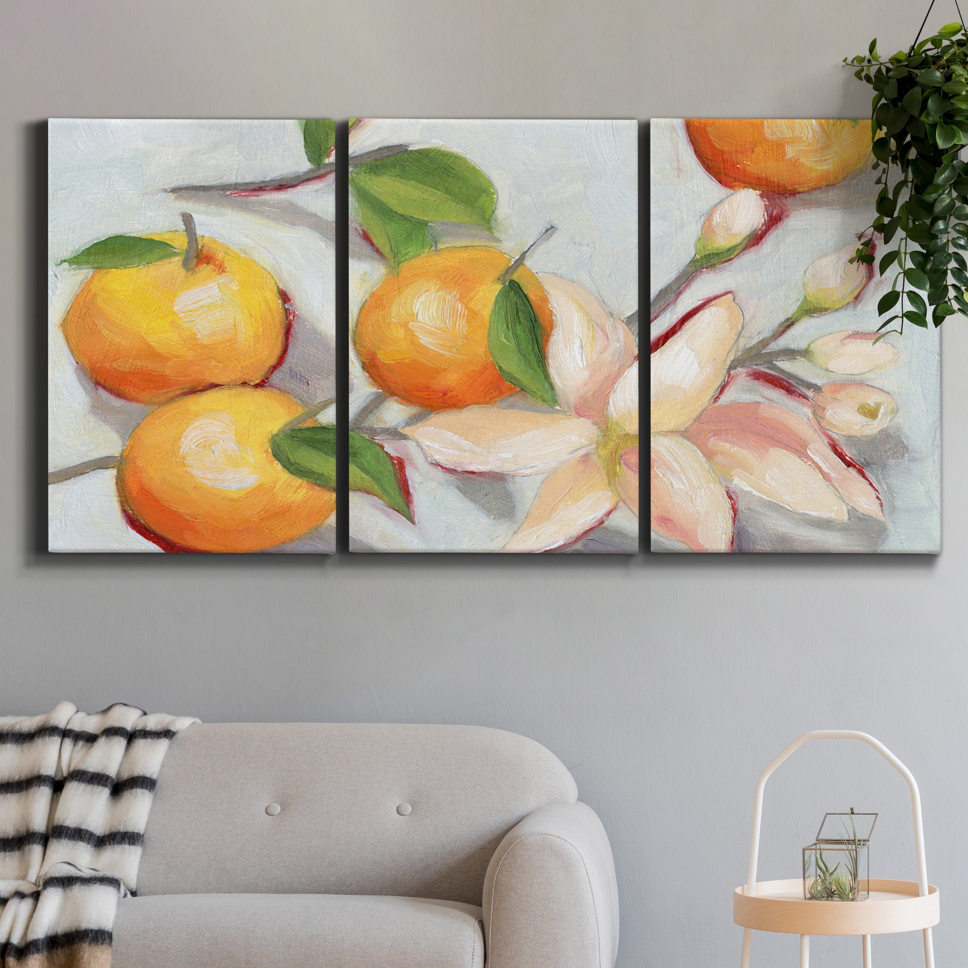 Three-panel canvas wall art featuring bright tangerine still life blossoms, displayed in a modern living room above a sofa.