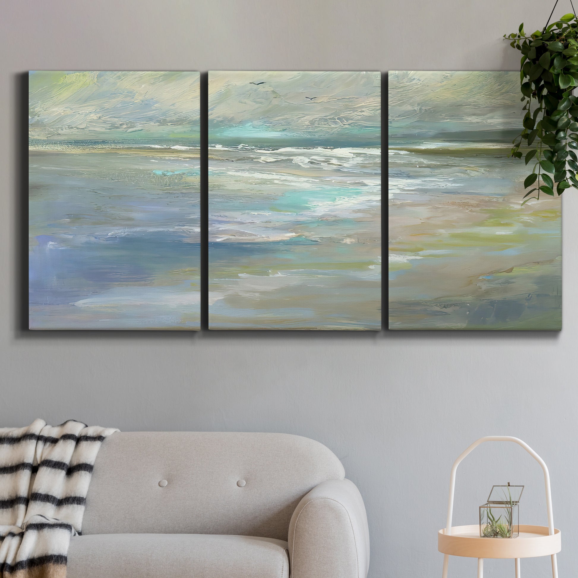 Three-panel canvas wall art featuring soft coastal beach light landscape, displayed in a modern living room above a sofa.