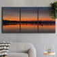 Three-panel canvas wall art featuring glowing sunset over water, displayed in a modern living room above a sofa.