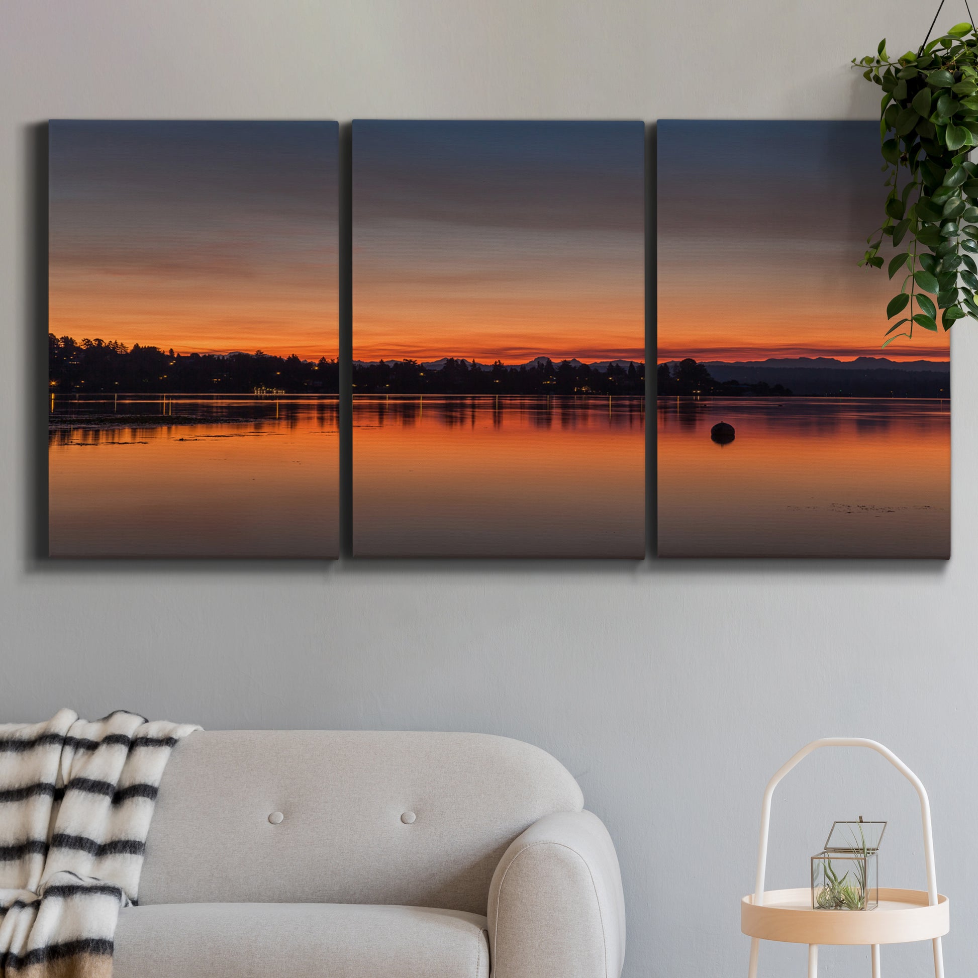 Three-panel canvas wall art featuring glowing sunset over water, displayed in a modern living room above a sofa.