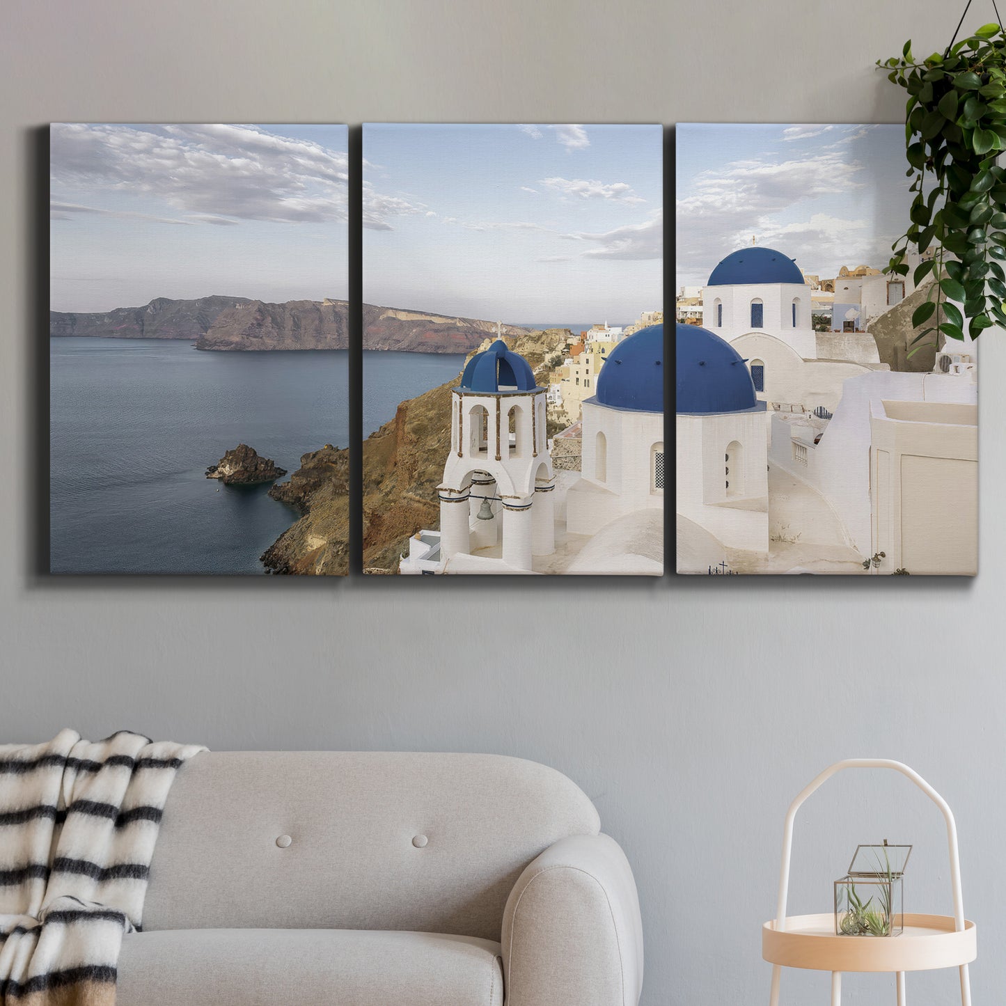 Three-panel canvas wall art featuring white buildings overlooking sea cliffs, displayed in a modern living room above a sofa.