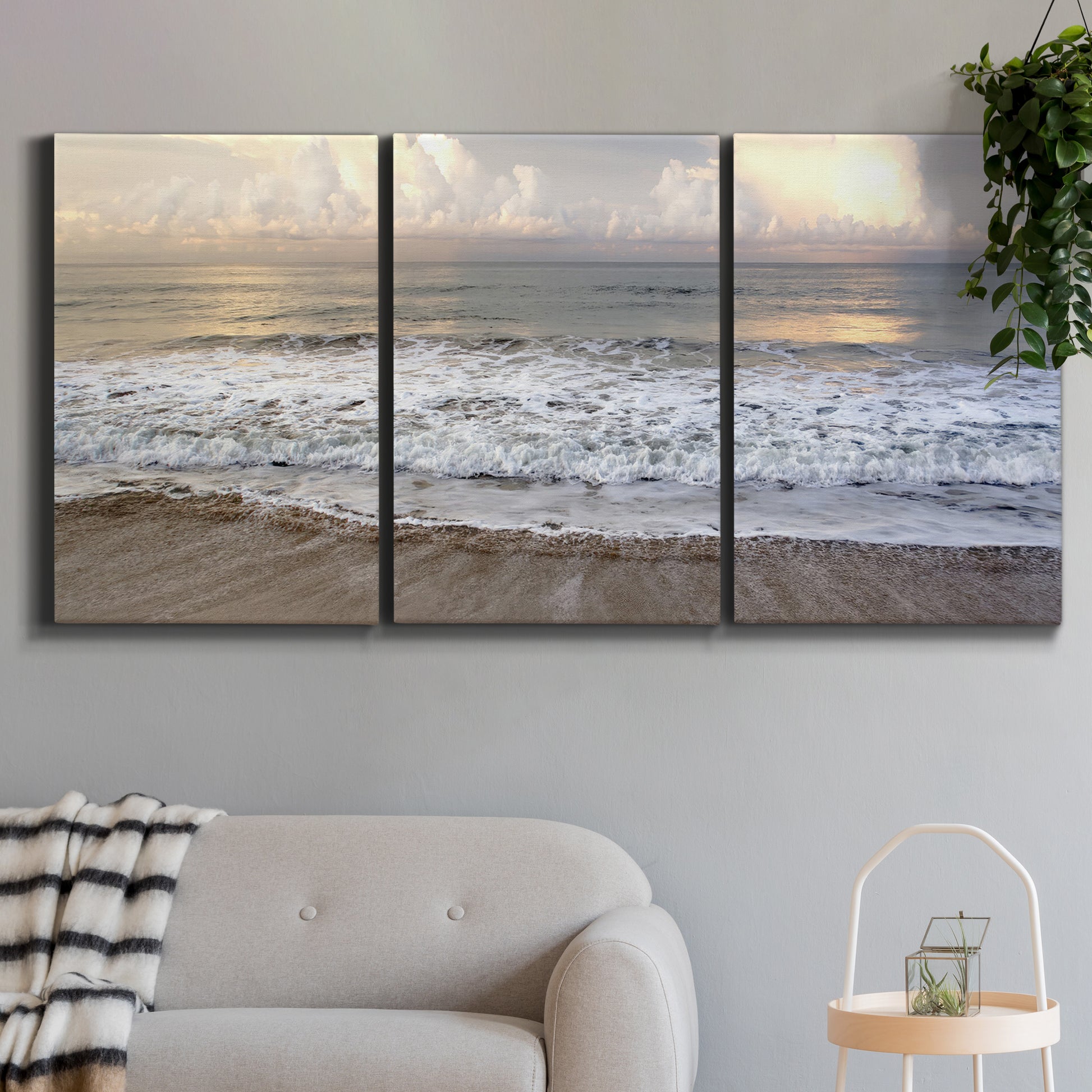 Three-panel canvas wall art featuring calm coastal shoreline seascape, displayed in a modern living room above a sofa.