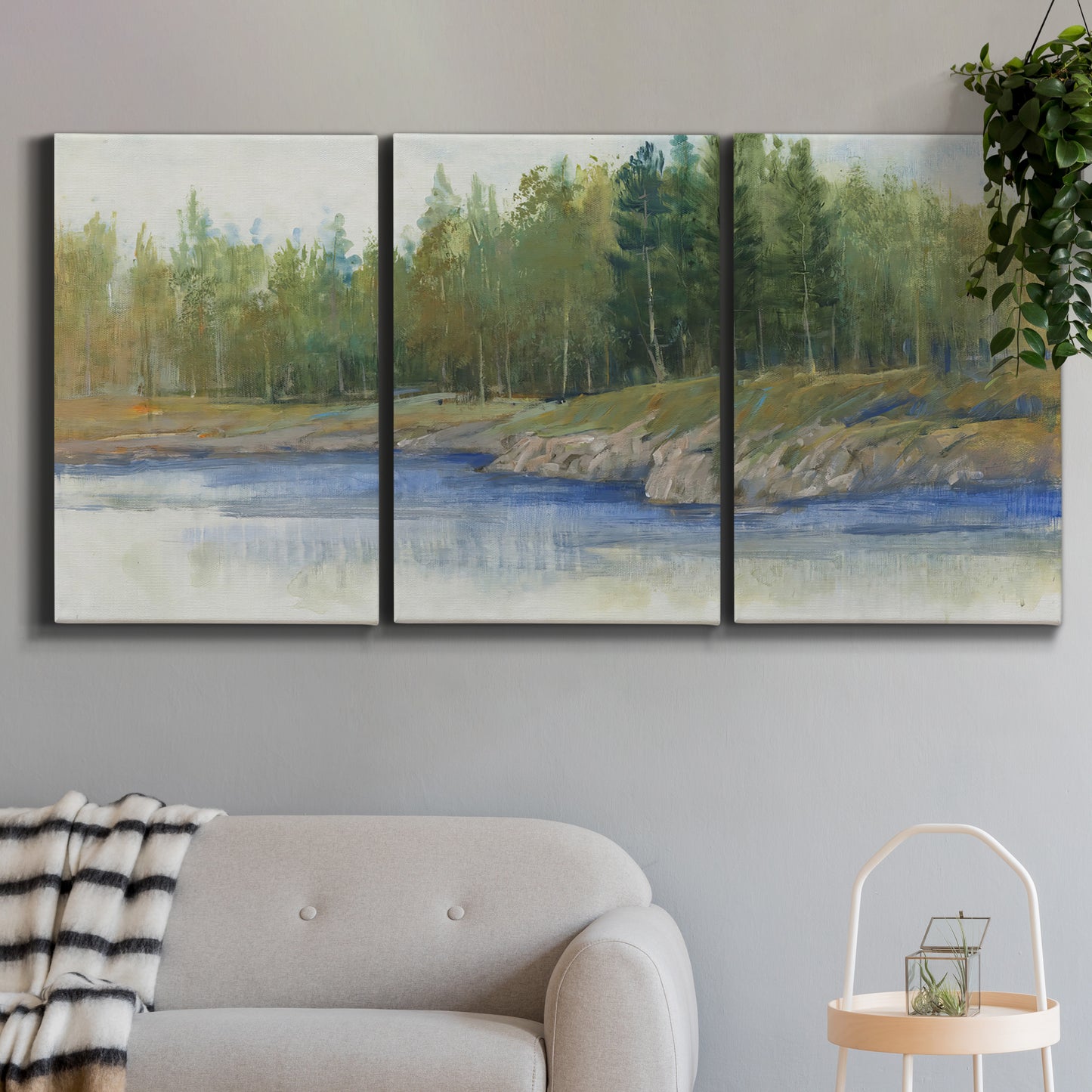 Three-panel canvas wall art featuring riverbank landscape with trees, displayed in a modern living room above a sofa.