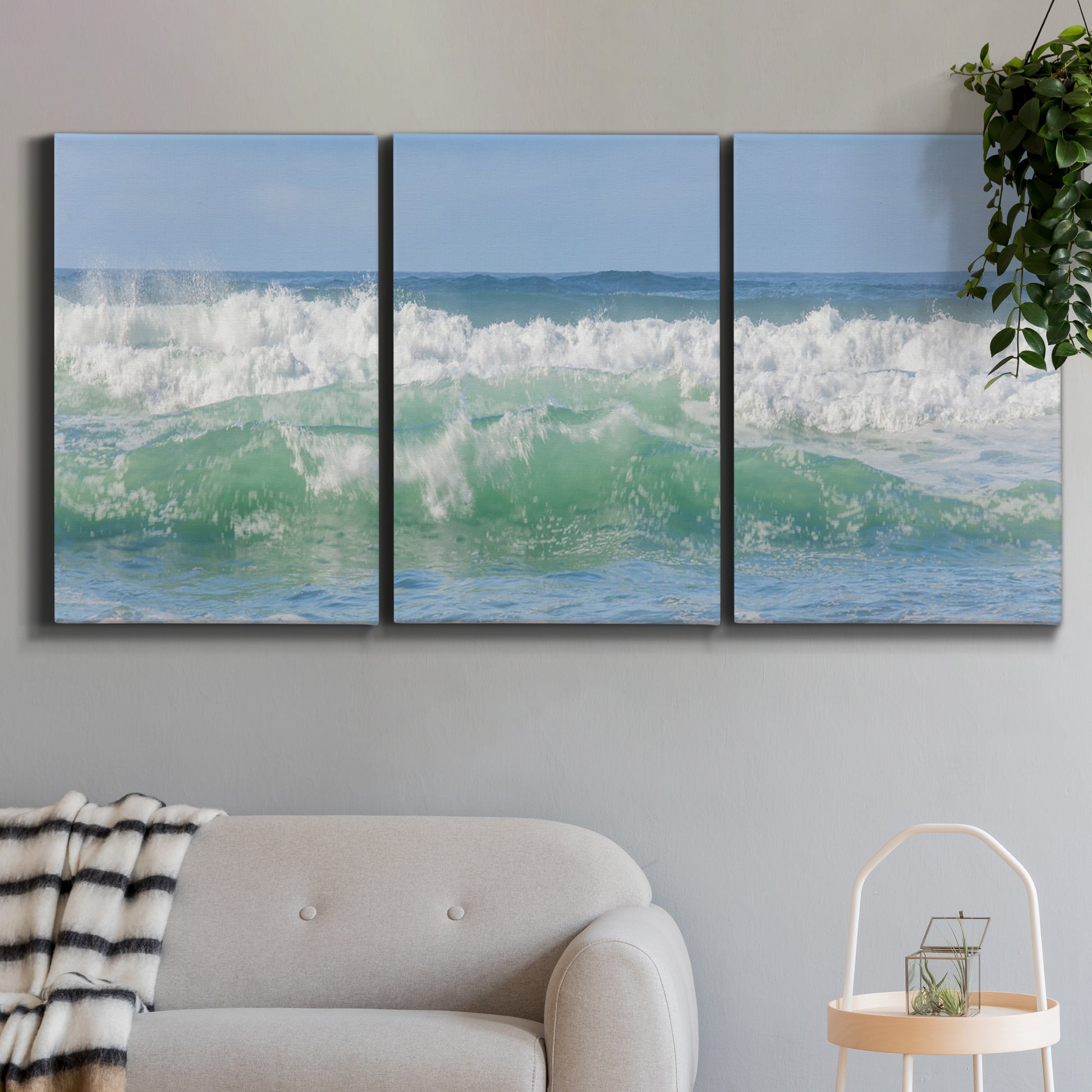 Three-panel canvas wall art featuring coastal waves breaking ashore, displayed in a modern living room above a sofa.