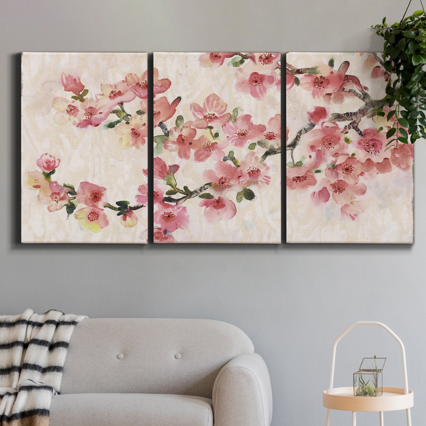 Three-panel canvas wall art featuring blooming cherry blossom branches, displayed in a modern living room above a sofa.