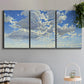 Three-panel canvas wall art featuring whimsical cloud filled sky landscape, displayed in a modern living room above a sofa.