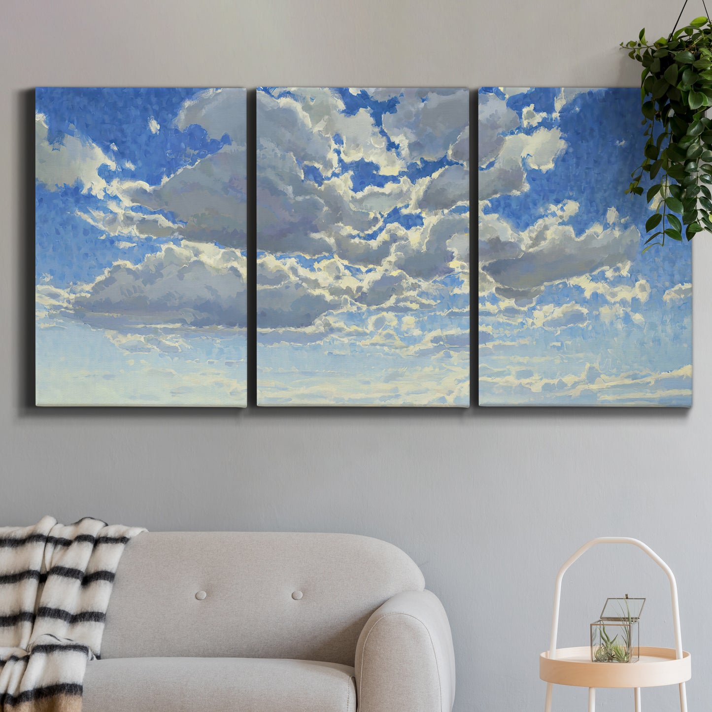 Three-panel canvas wall art featuring whimsical cloud filled sky landscape, displayed in a modern living room above a sofa.