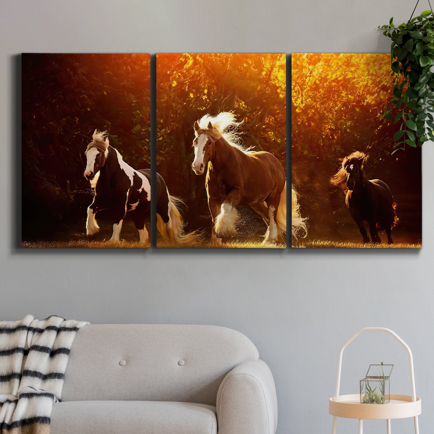 Three-panel canvas wall art featuring running horses across open field, displayed in a modern living room above a sofa.