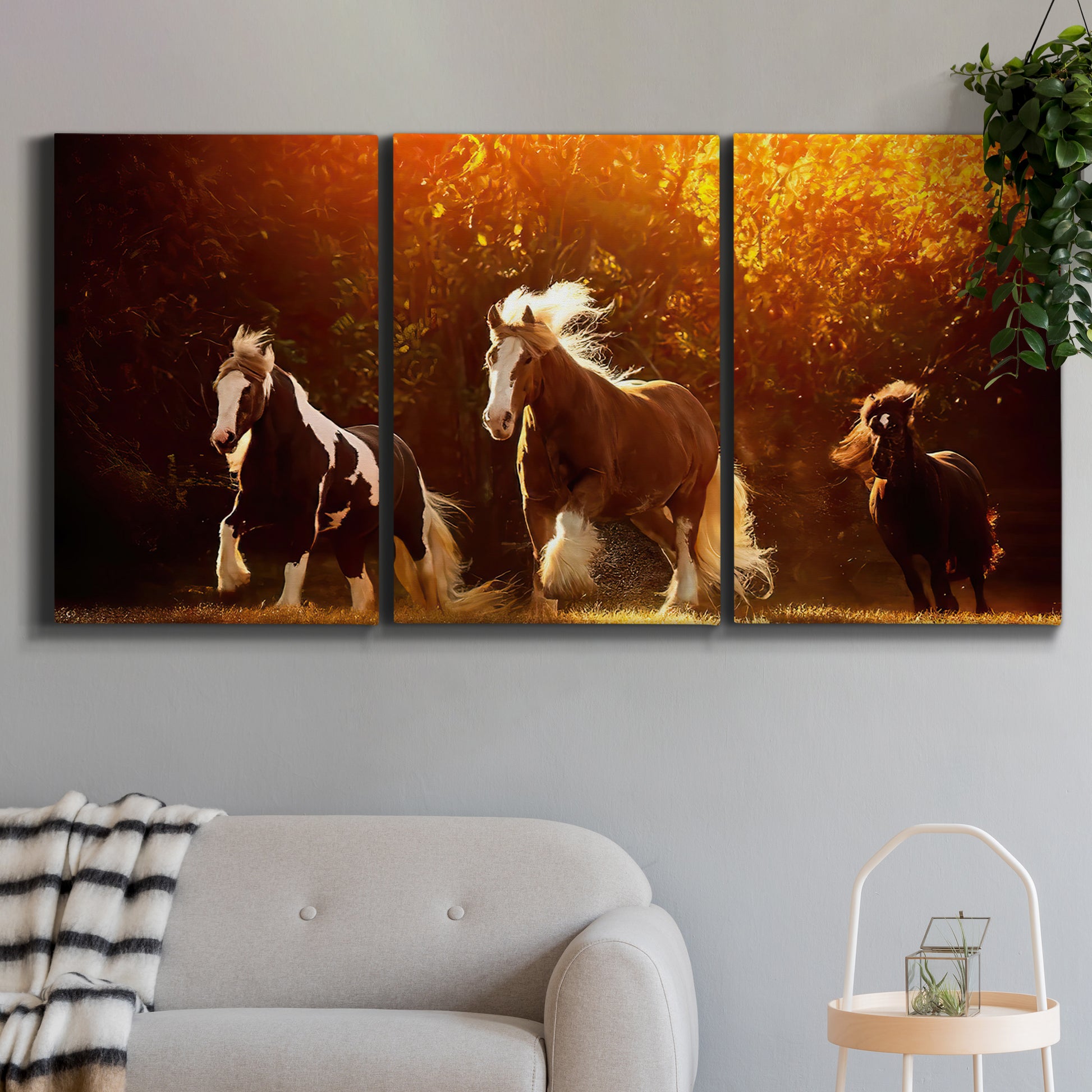 Three-panel canvas wall art featuring running horses across open field, displayed in a modern living room above a sofa.