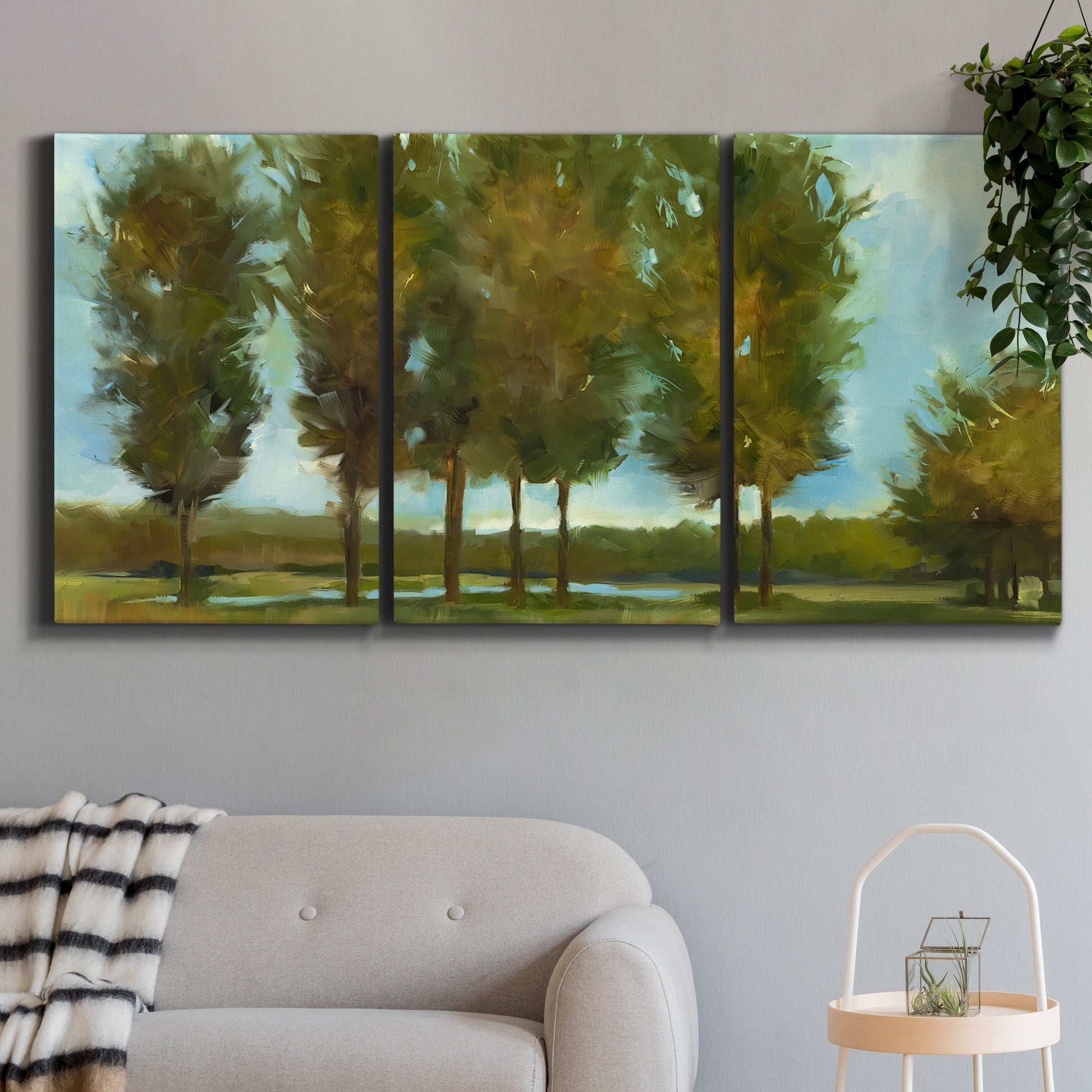 Three-panel canvas wall art featuring tall trees lining open landscape, displayed in a modern living room above a sofa.