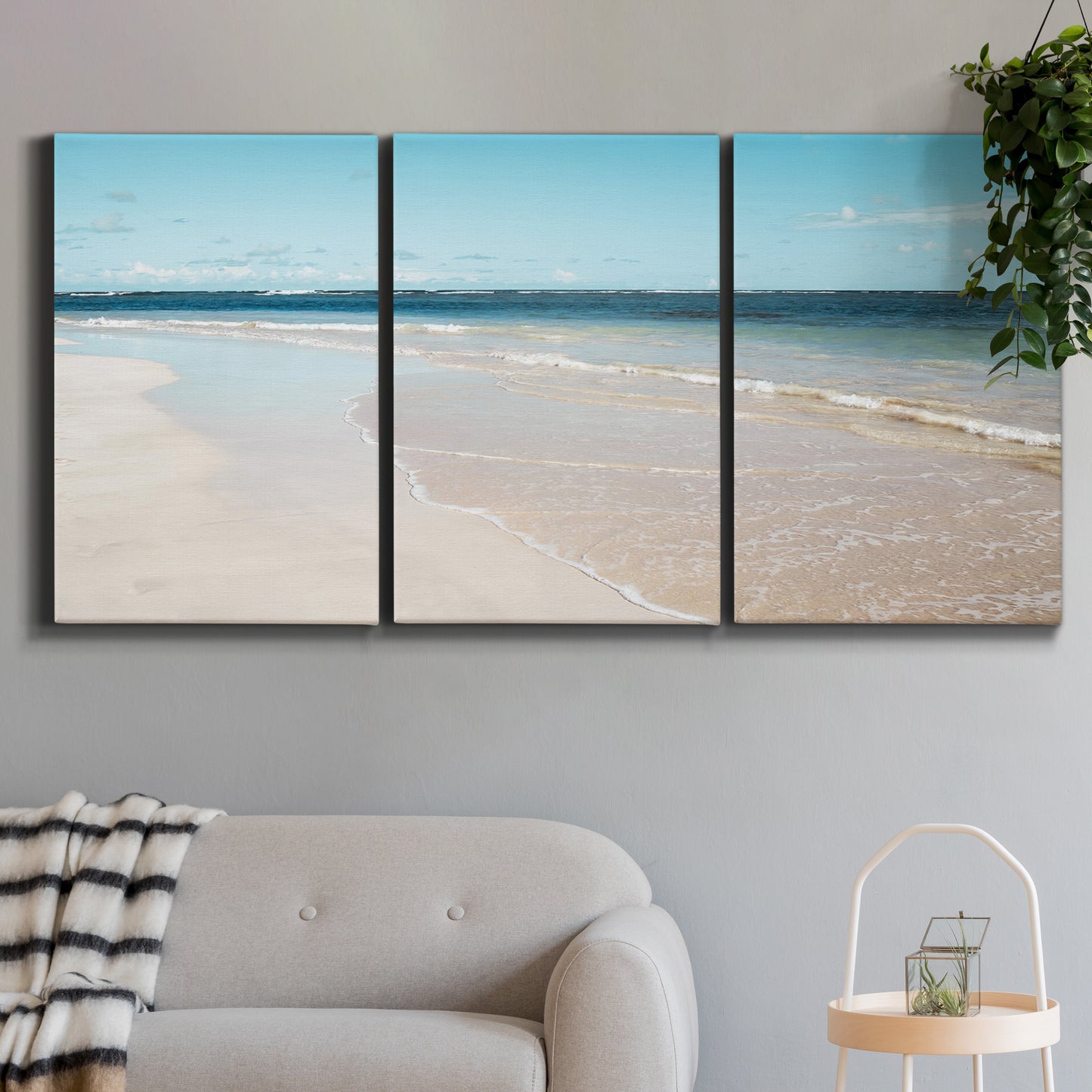 Three-panel canvas wall art featuring white sand beach with gentle waves, displayed in a modern living room above a sofa.