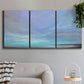 Three-panel canvas wall art featuring coastal shoreline with gentle surf, displayed in a modern living room above a sofa.