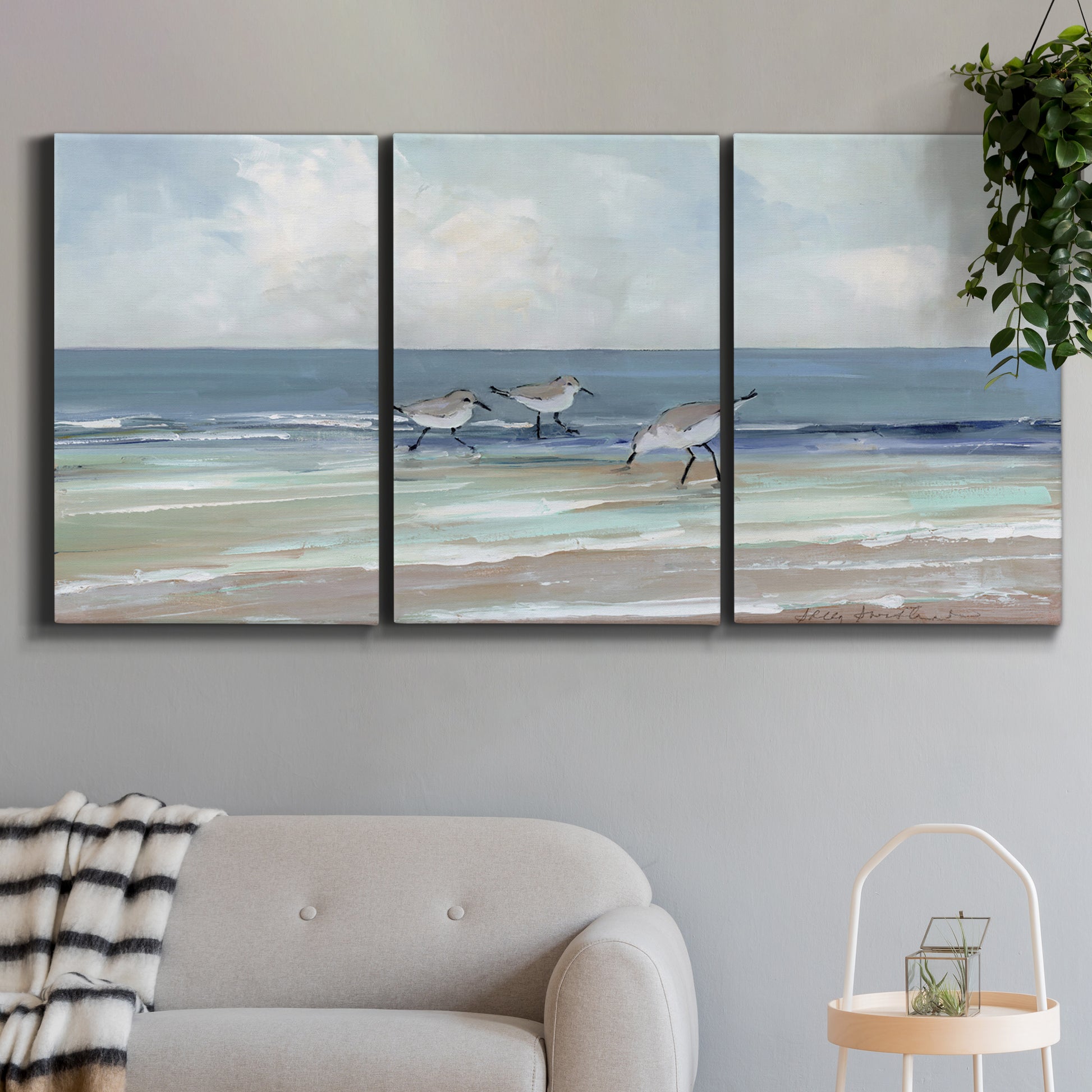 Three-panel canvas wall art featuring shore birds searching along beach, displayed in a modern living room above a sofa.