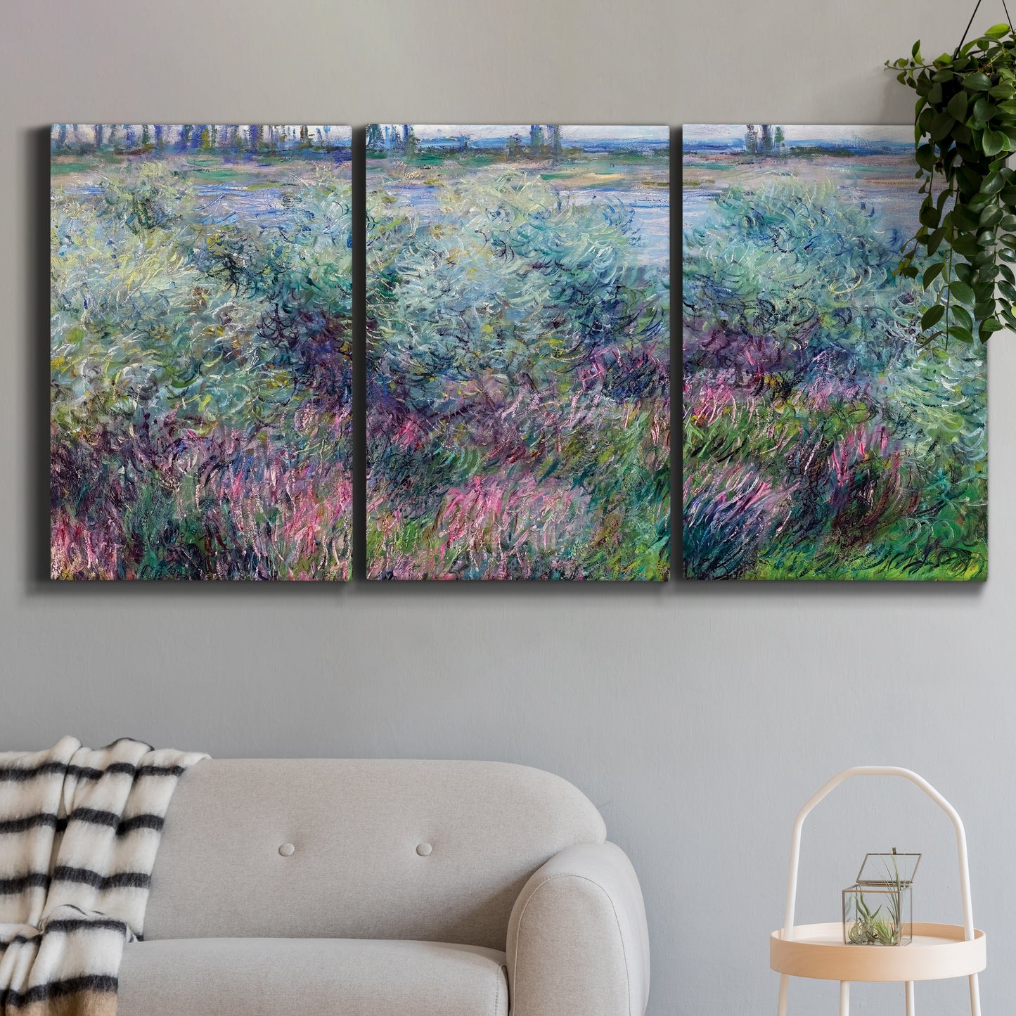 Three-panel canvas wall art featuring flowered riverbank with trees, displayed in a modern living room above a sofa.