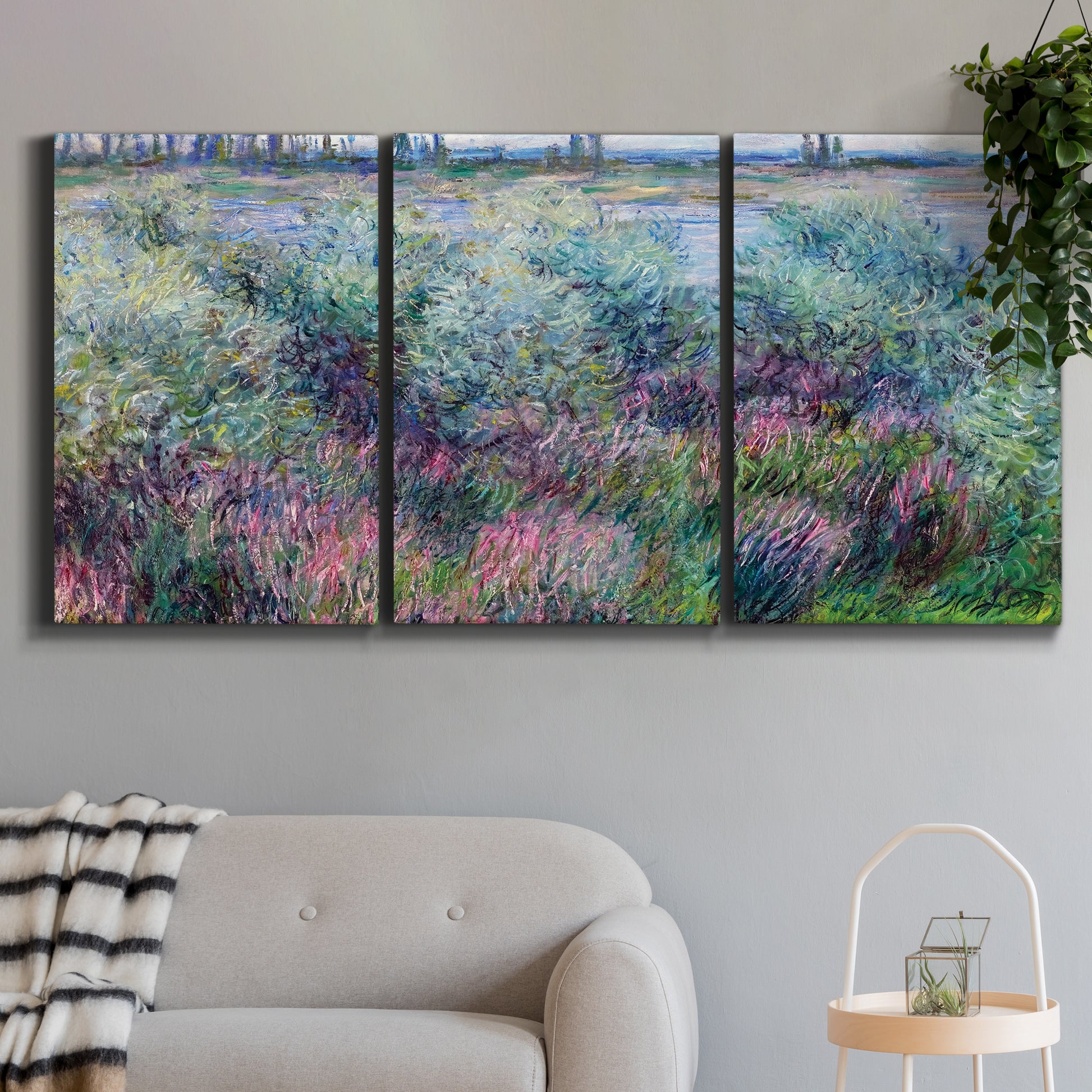 Three-panel canvas wall art featuring flowered riverbank with trees, displayed in a modern living room above a sofa.