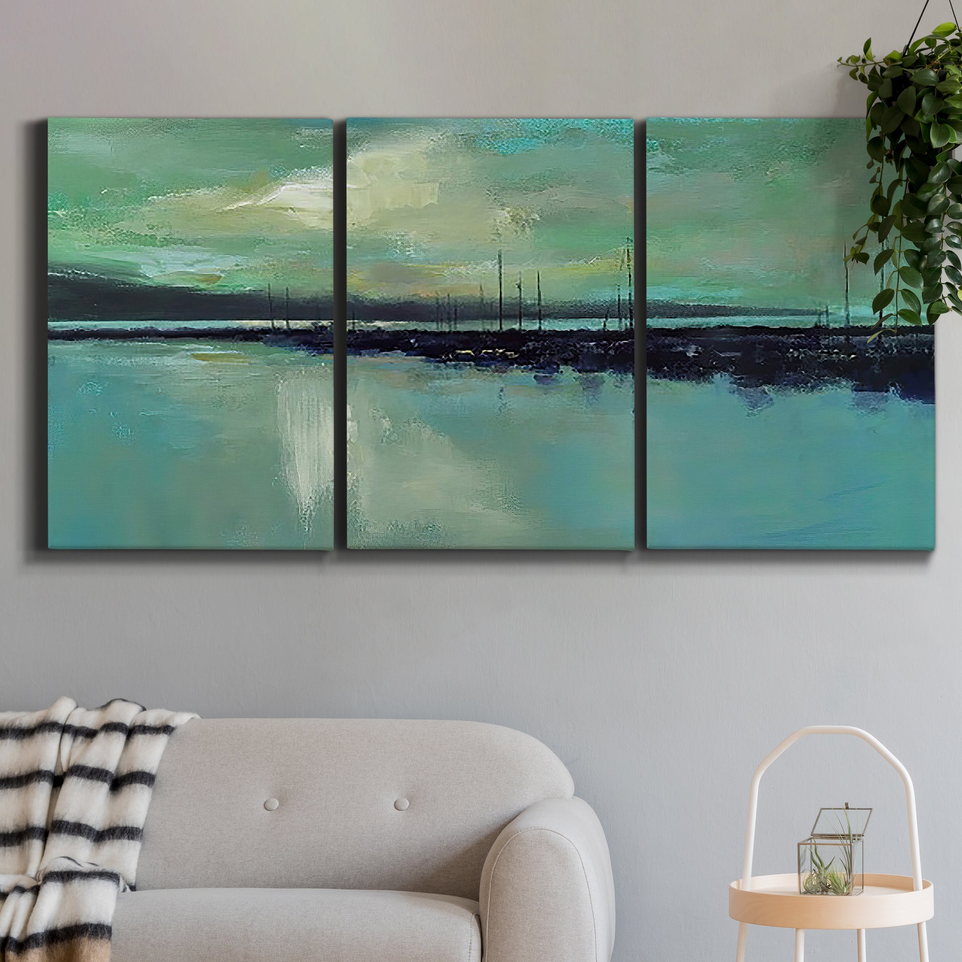 Three-panel canvas wall art featuring calm harbor water with glowing horizon, displayed in a modern living room above a sofa.