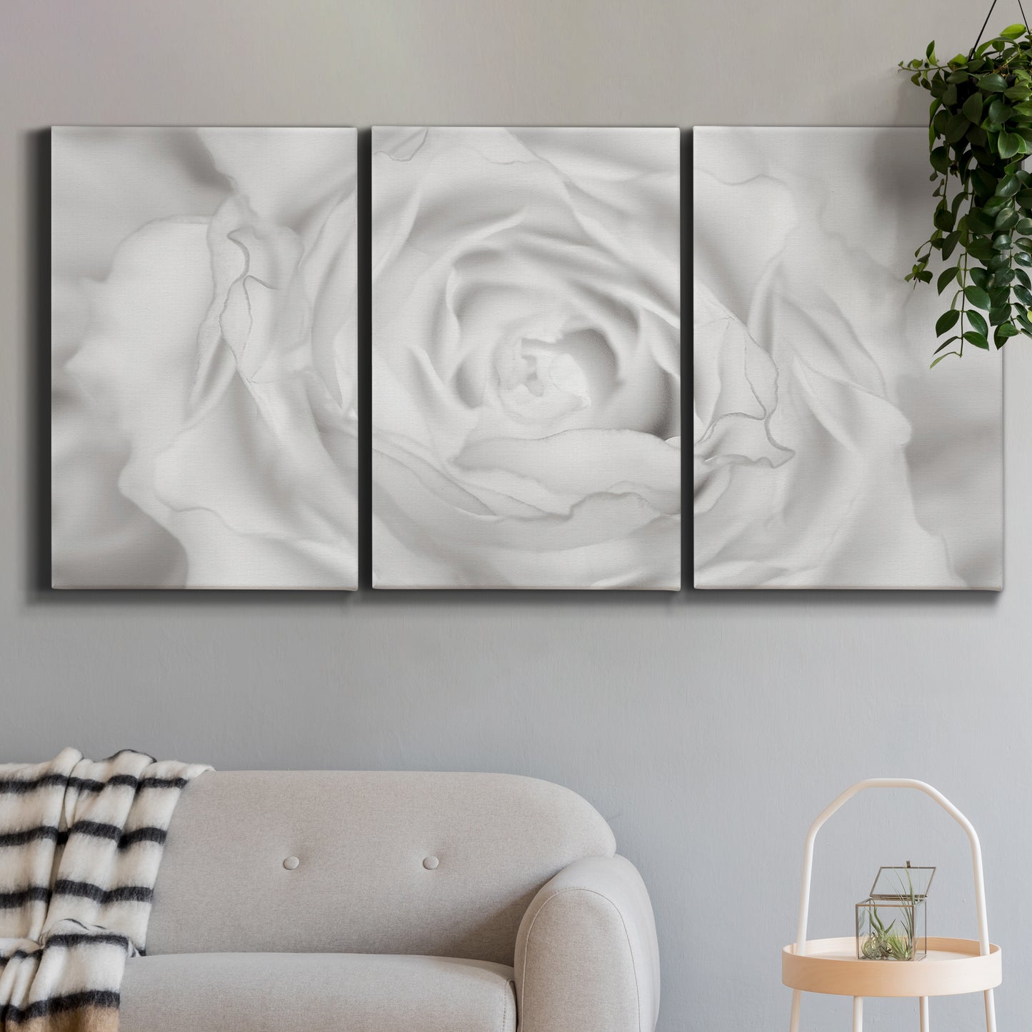 Three-panel canvas wall art featuring monochrome rose study photograph, displayed in a modern living room above a sofa.