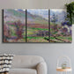 Three-panel canvas wall art featuring cliffside cottage overlooking sea, displayed in a modern living room above a sofa.