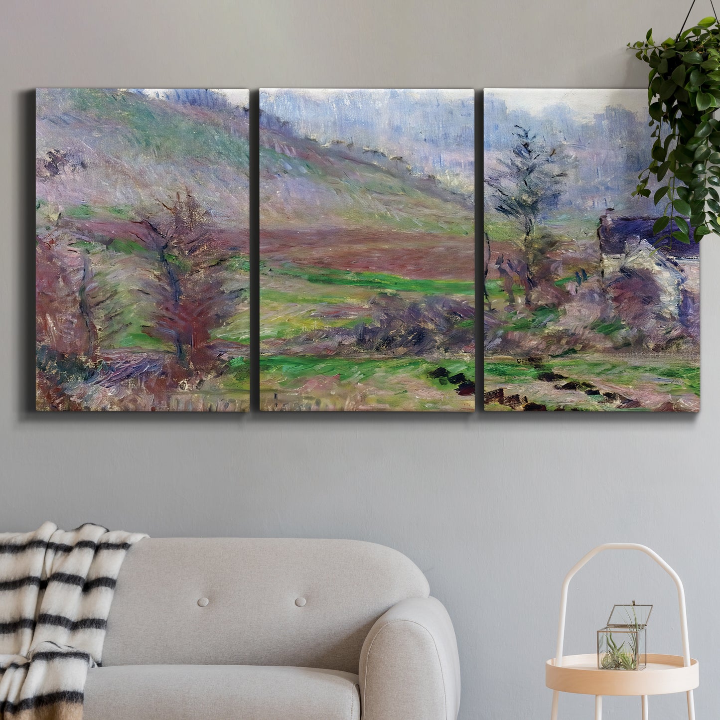 Three-panel canvas wall art featuring cliffside cottage overlooking sea, displayed in a modern living room above a sofa.