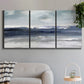 Three-panel canvas wall art featuring abstract coastal tones and movement, displayed in a modern living room above a sofa.
