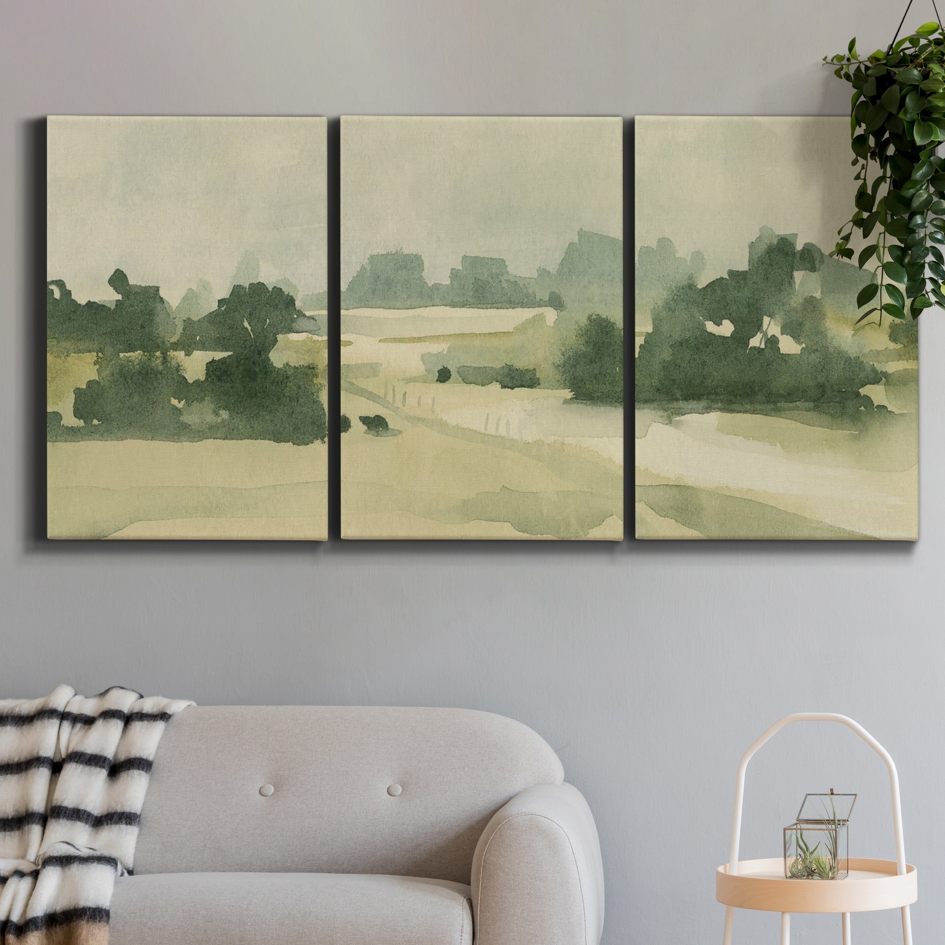 Three-panel canvas wall art featuring pasture landscape in soft watercolor, displayed in a modern living room above a sofa.