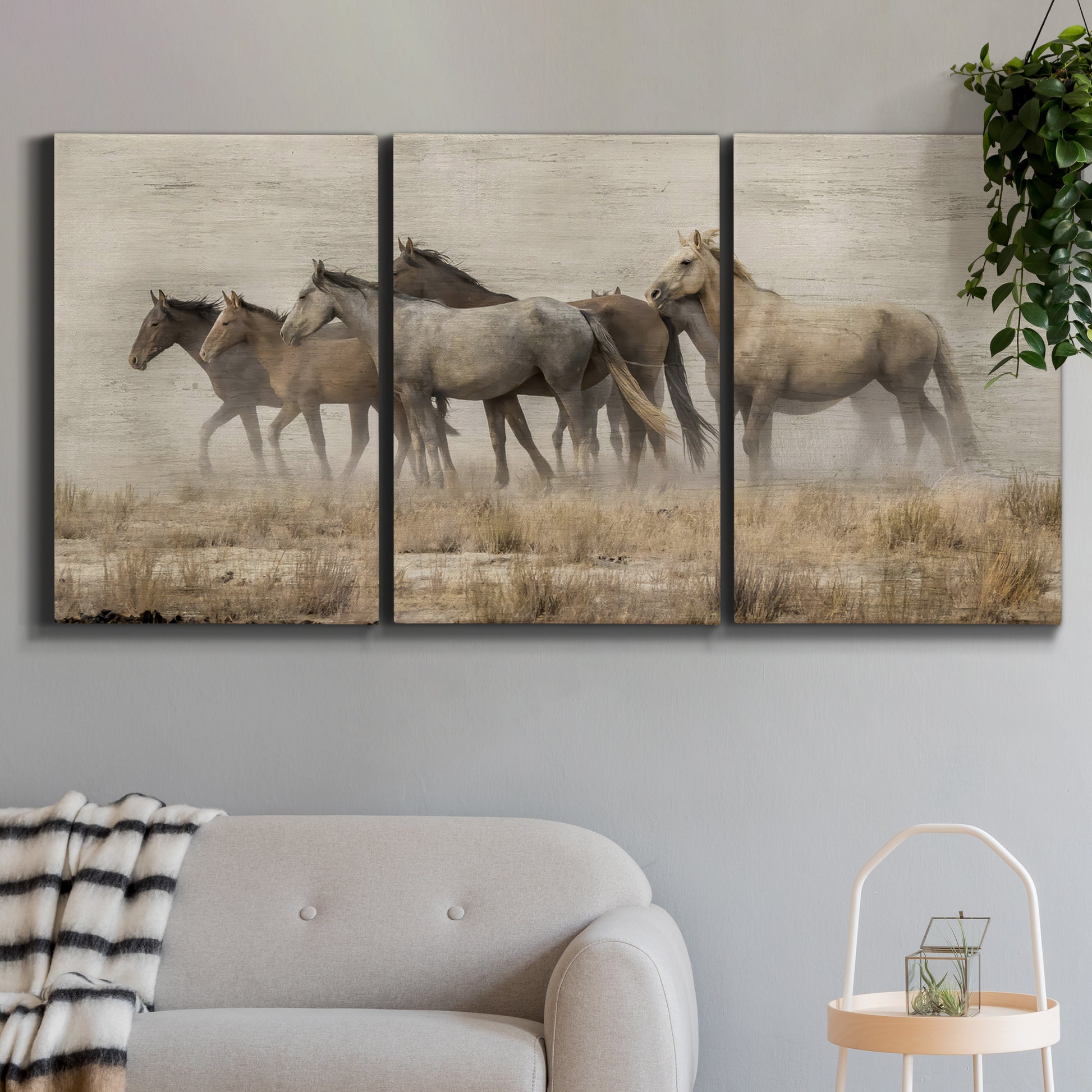 Three-panel canvas wall art featuring wild horses roaming open terrain, displayed in a modern living room above a sofa.