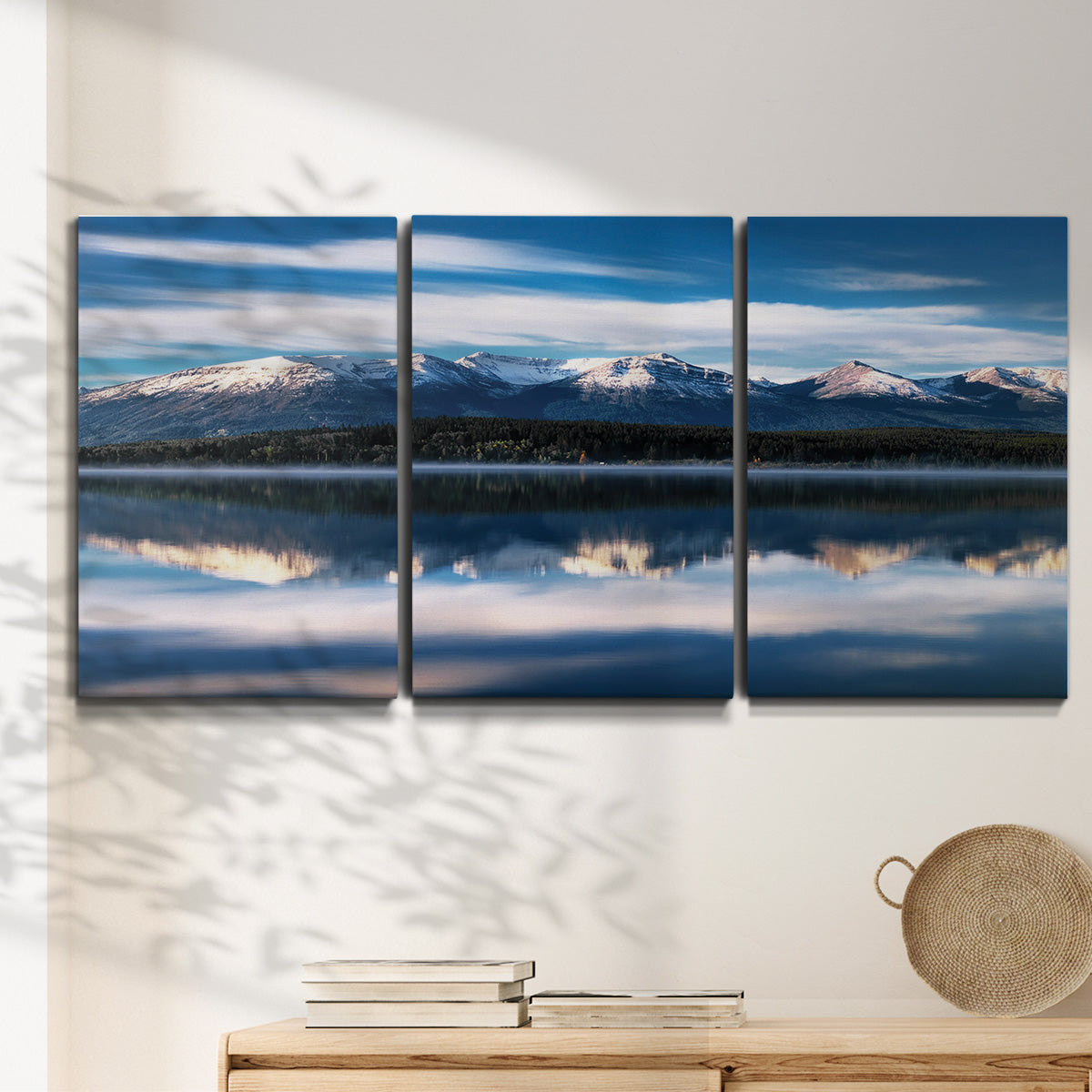 Three-panel canvas wall art featuring calm lake beneath mountains photograph, displayed in a minimalist living room above a console table.