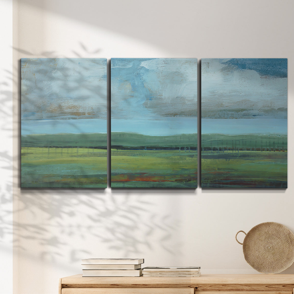 Three-panel canvas wall art featuring wide valley landscape with rolling hills, displayed in a minimalist living room above a console table.