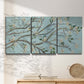 Three-panel canvas wall art featuring blue sky with flowering branches, displayed in a minimalist living room above a console table.