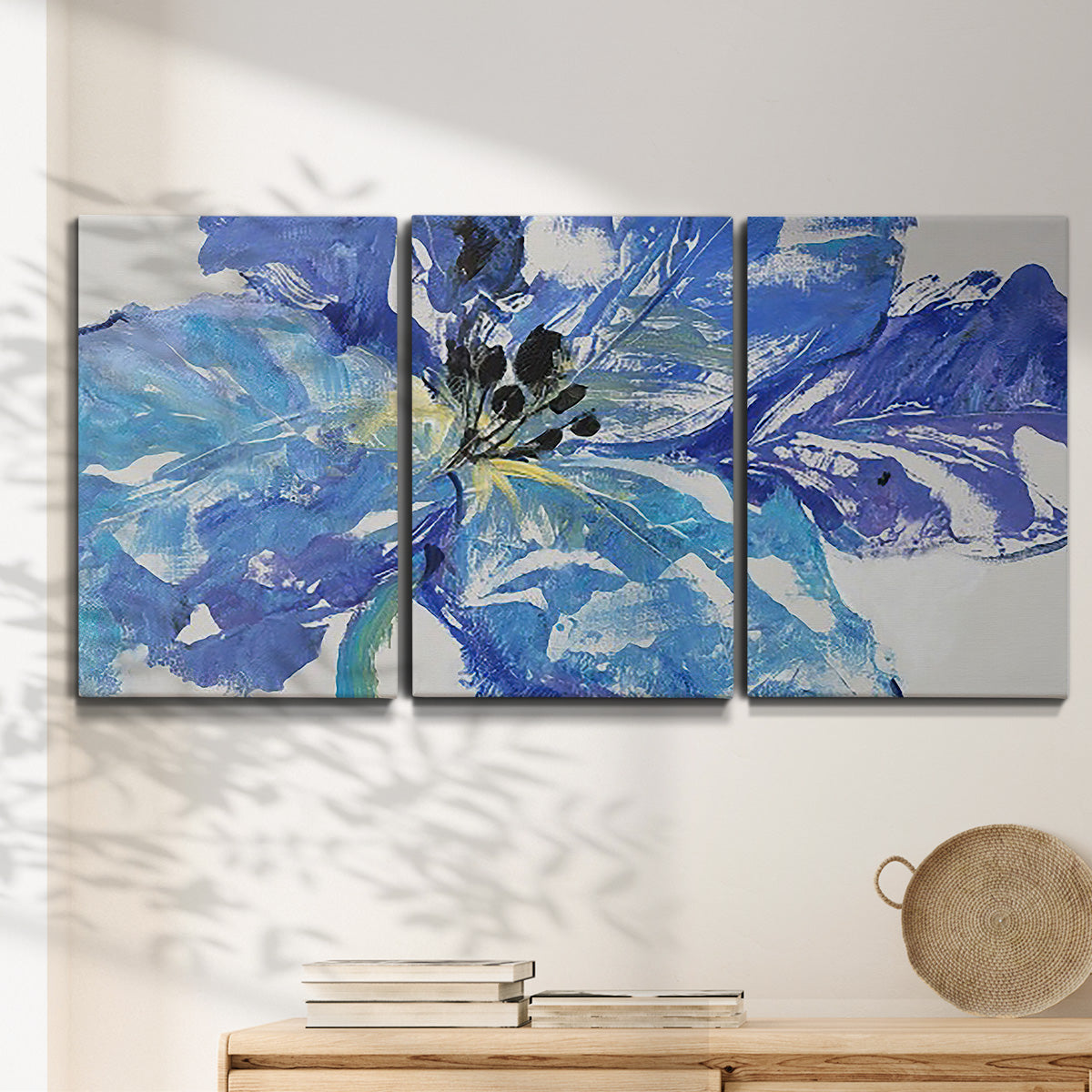 Three-panel canvas wall art featuring blue floral botanical close up, displayed in a minimalist living room above a console table.