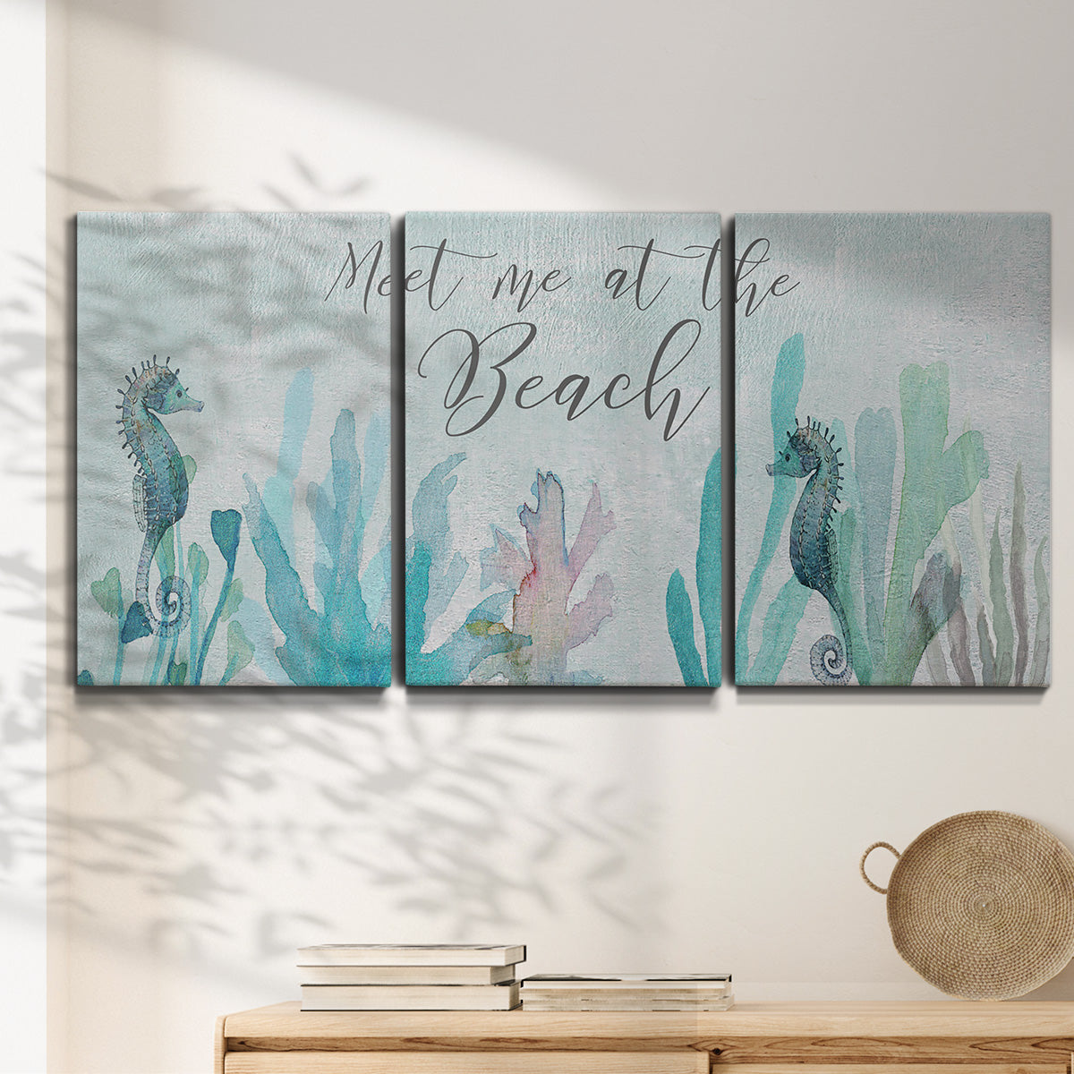 Three-panel canvas wall art featuring coastal typography with seahorses, displayed in a minimalist living room above a console table.