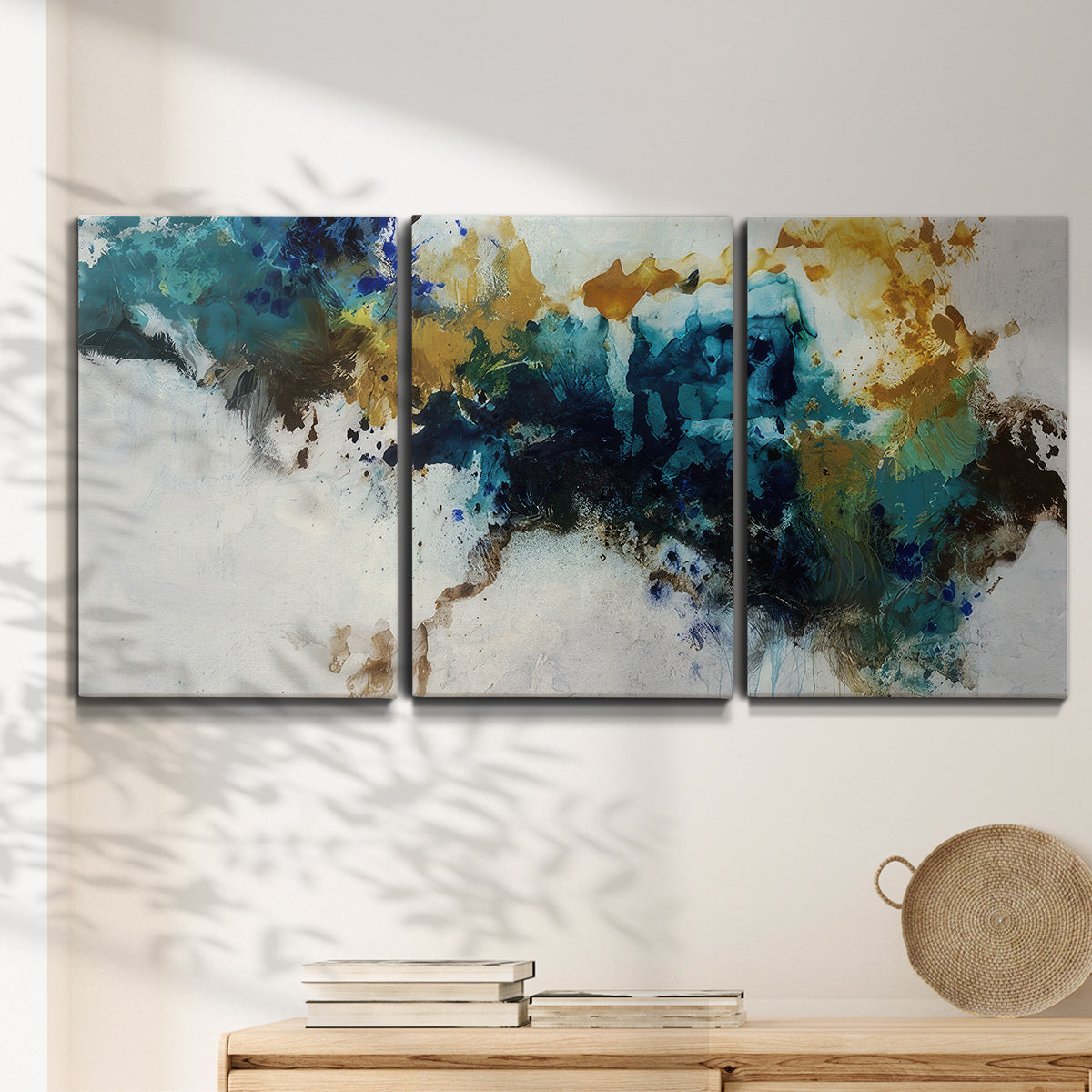 Three-panel canvas wall art featuring teal abstract paint splatter, displayed in a minimalist living room above a console table.