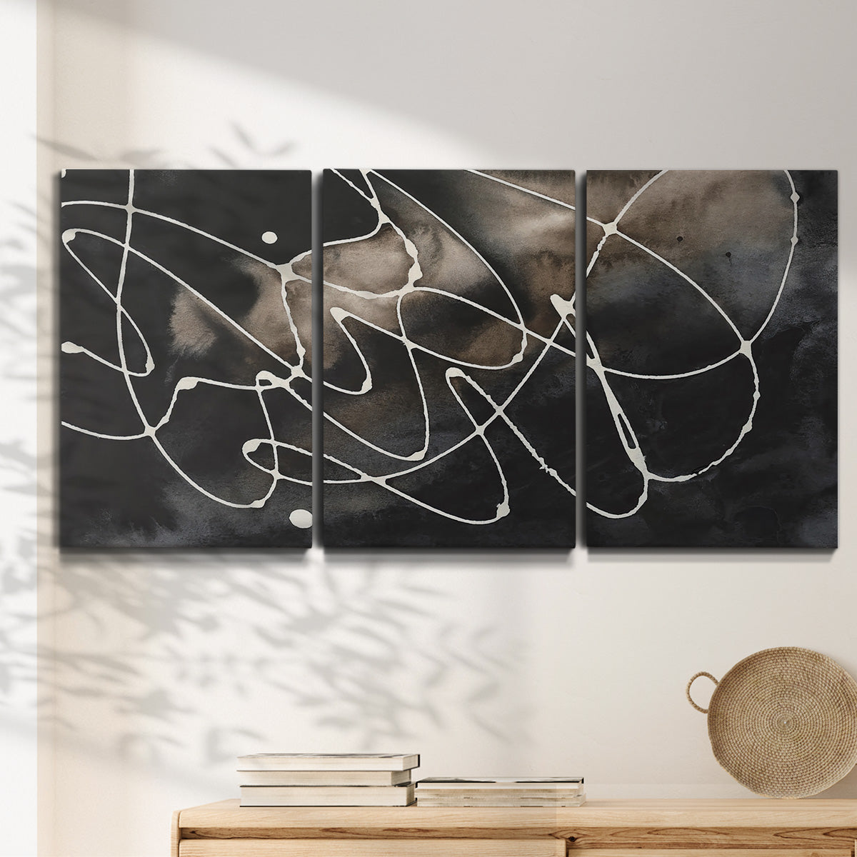 Three-panel canvas wall art featuring dark swirling abstract motion, displayed in a minimalist living room above a console table.