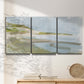 Three-panel canvas wall art featuring coastal cove with calm water, displayed in a minimalist living room above a console table.